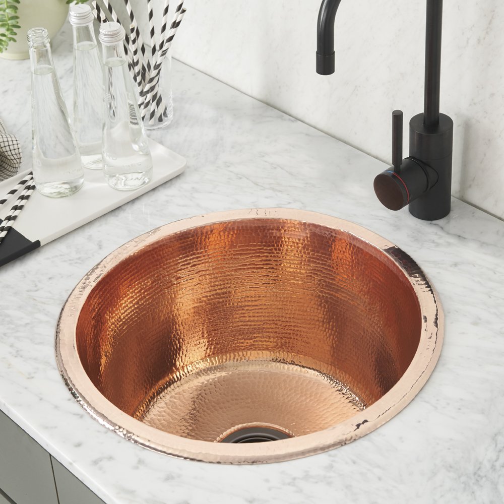 Polished copper round prep sink with hammered texture installed in marble countertop next to black faucet.