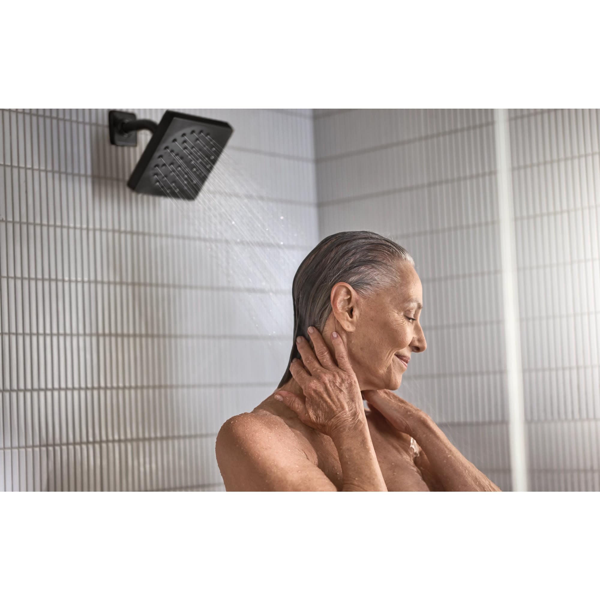 Black square showerhead with water stream mounted on shower wall above person bathing.