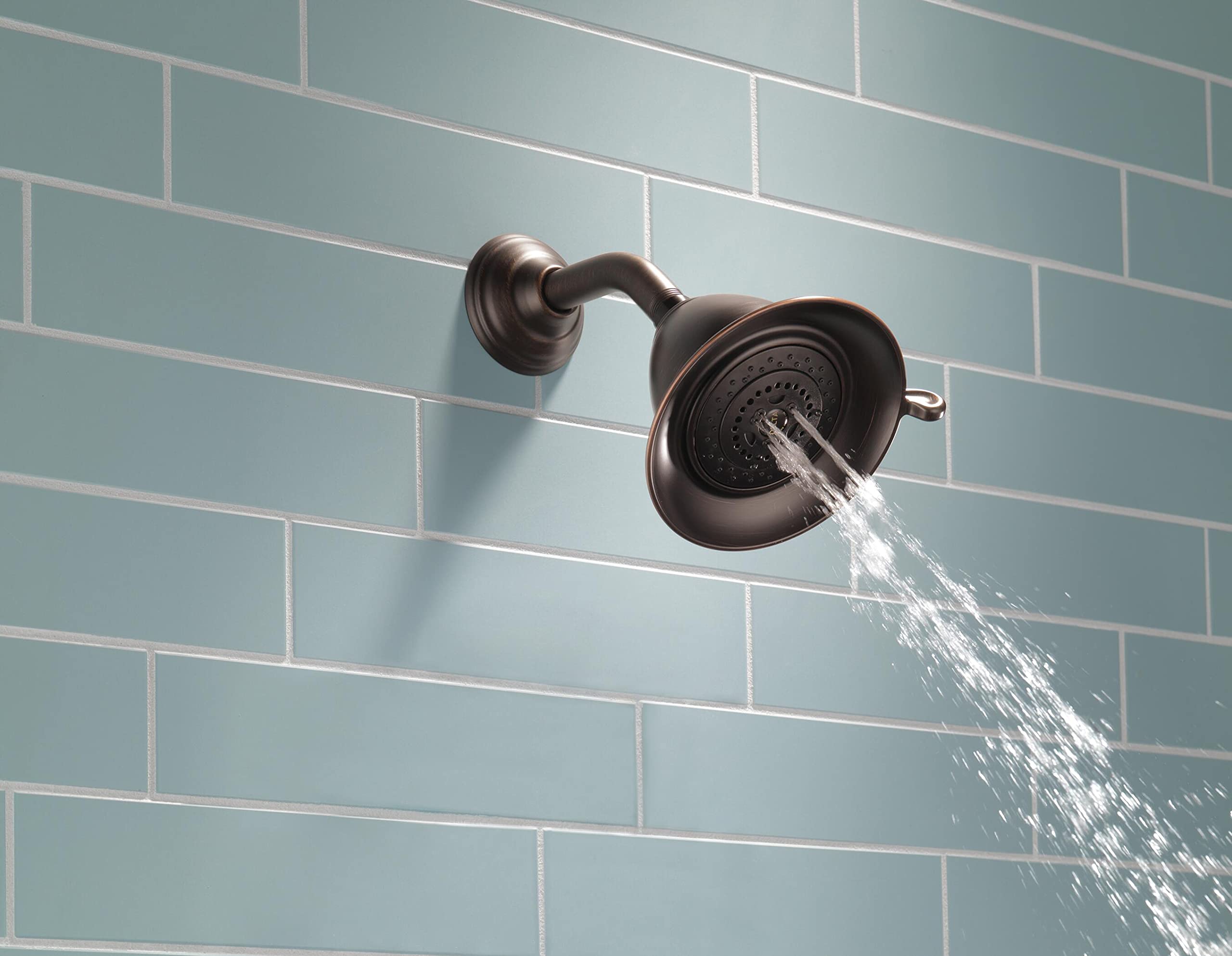 Chrome showerhead with curved arm mounted on tiled wall, water streaming from multiple jets.