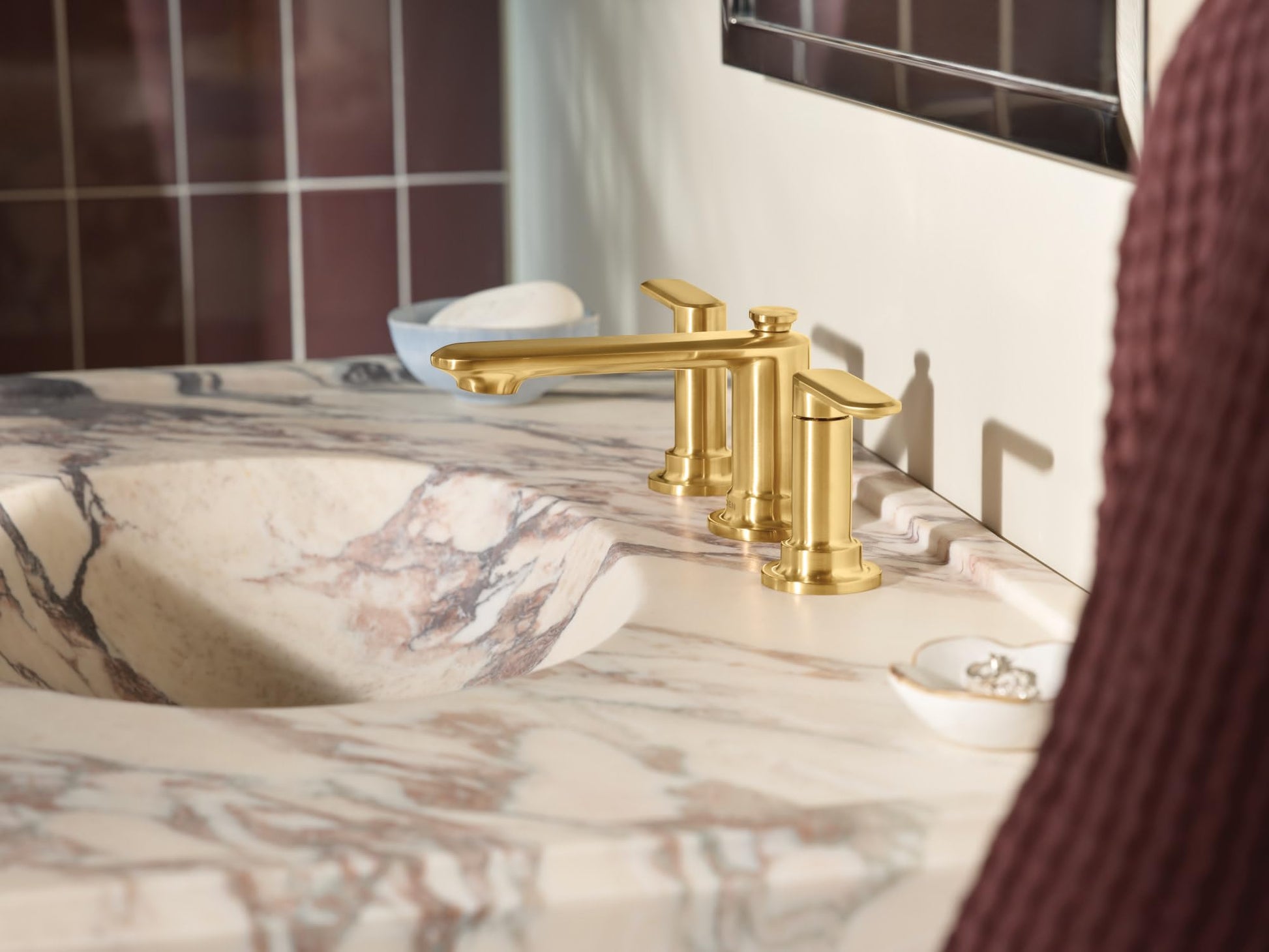 Brushed gold two-handle widespread bathroom faucet with curved spout installed on marble countertop.
