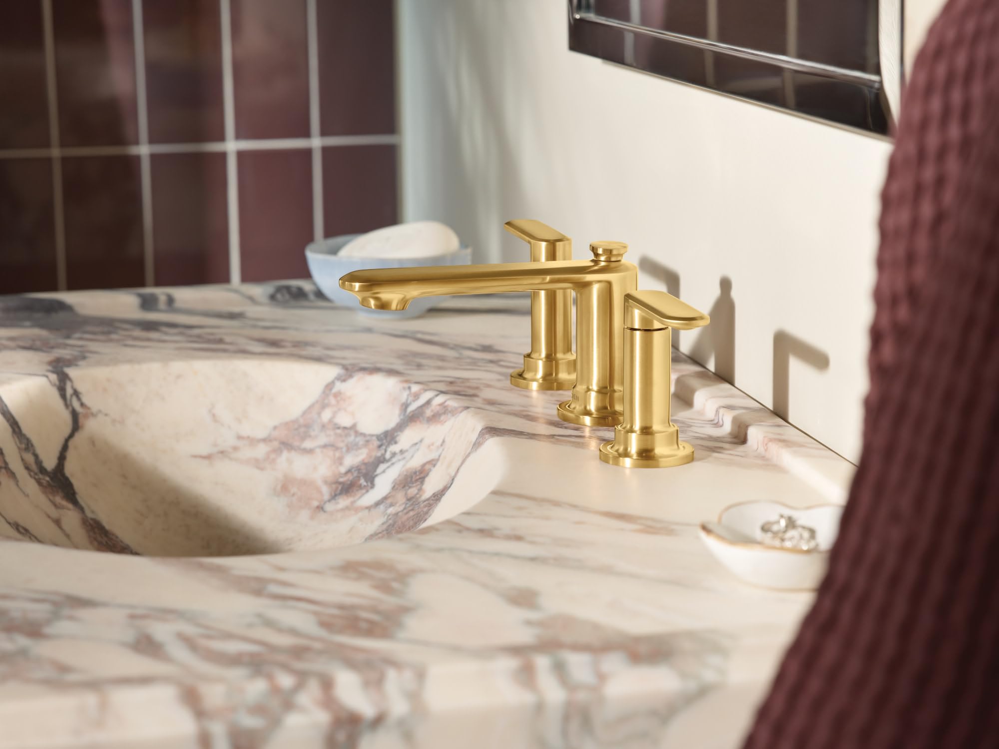 Brushed gold two-handle widespread bathroom faucet with curved spout installed on marble countertop.