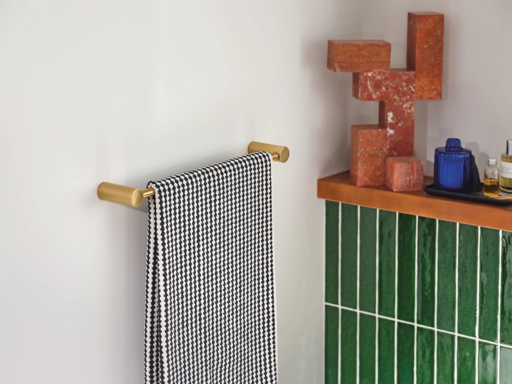 Brushed gold towel bar mounted on white wall with black and white patterned towel draped over it.