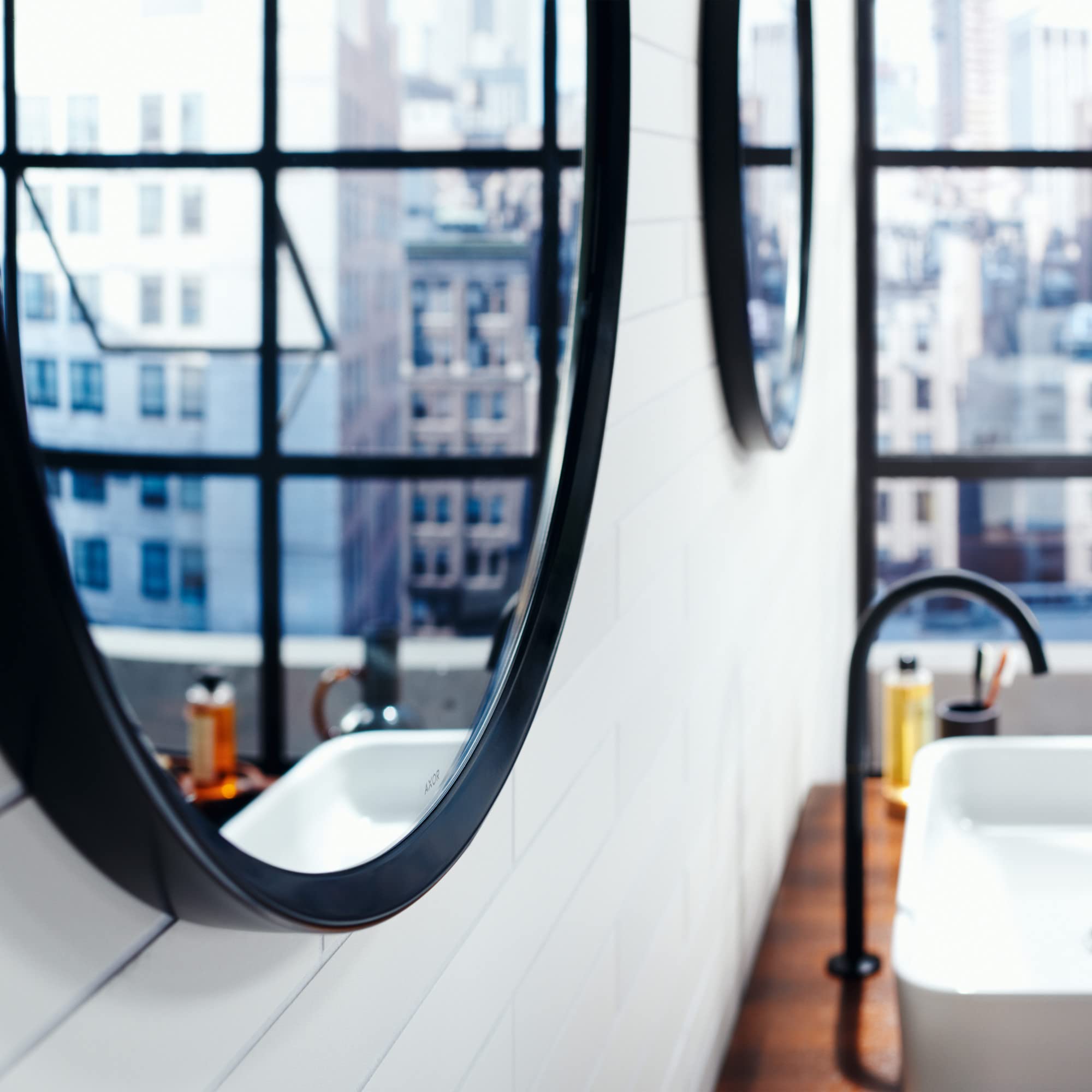 Round wall mirror with dark chrome frame mounted above bathroom sink counter.