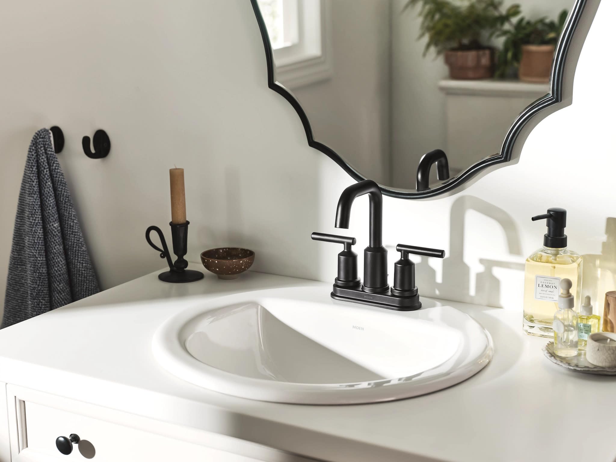 Matte black two-handle centerset bathroom faucet with curved spout installed on white round sink.