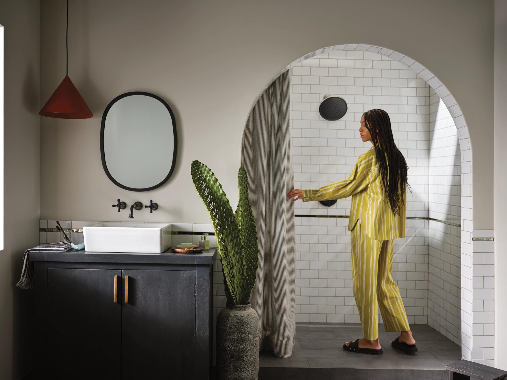Matte black single-handle shower trim kit mounted on white subway tile wall with showerhead and valve visible.
