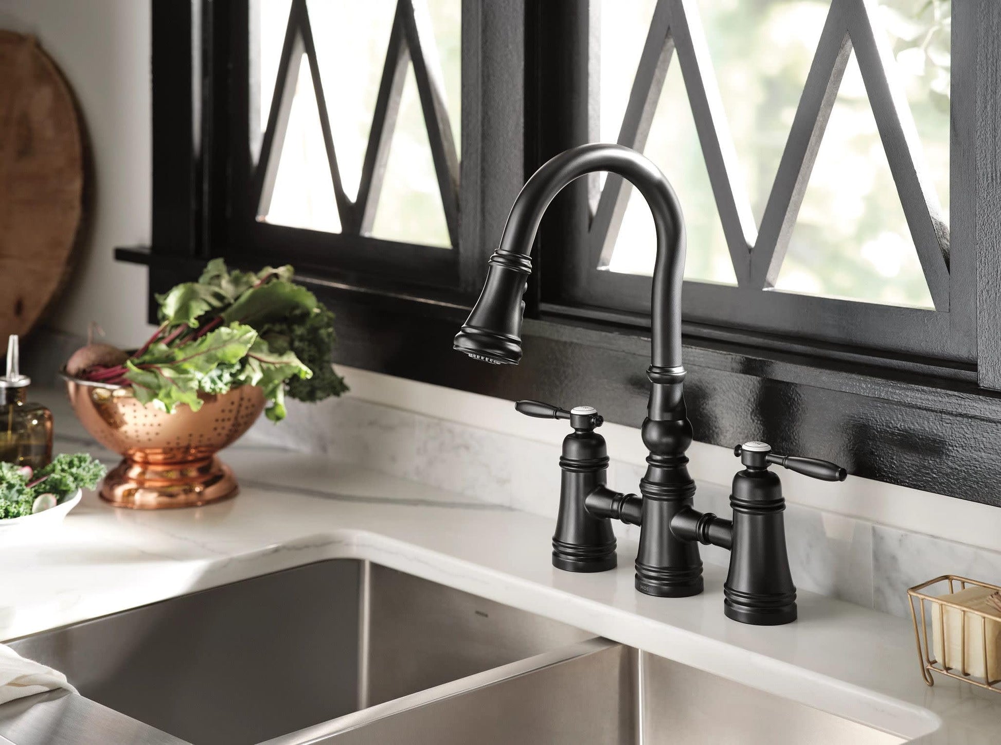 Matte black two-handle pulldown bridge kitchen faucet with curved spout over double basin sink.
