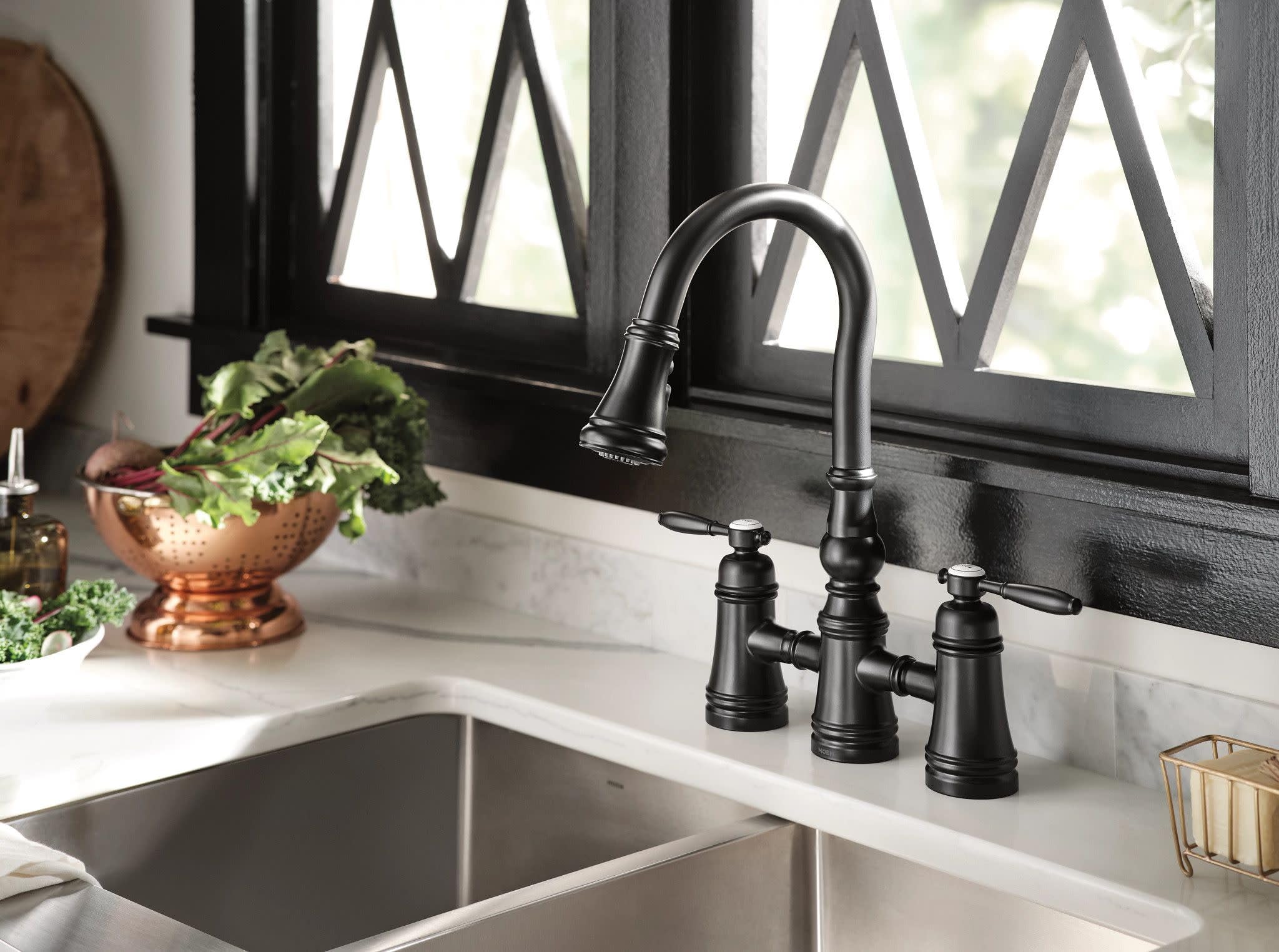 Matte black two-handle pulldown bridge kitchen faucet with curved spout over double basin sink.