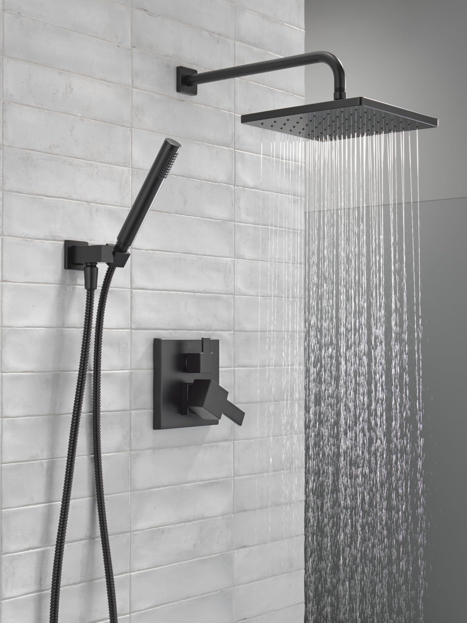 Matte black shower system with square raincan head, hand shower on hose, and wall-mounted control valve on white subway tile.