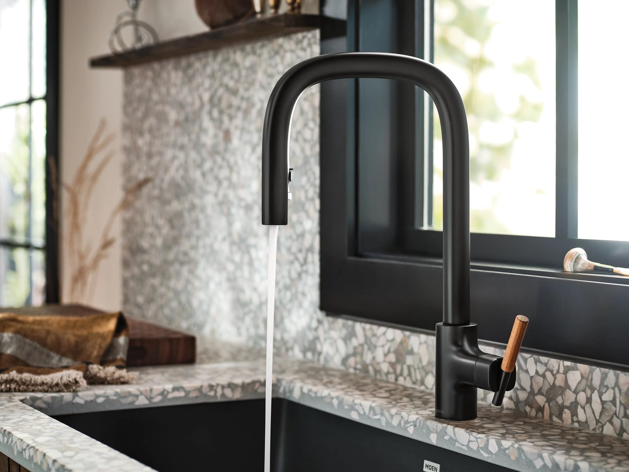 Matte black kitchen faucet with curved pulldown spout and wooden accent handle installed above sink.