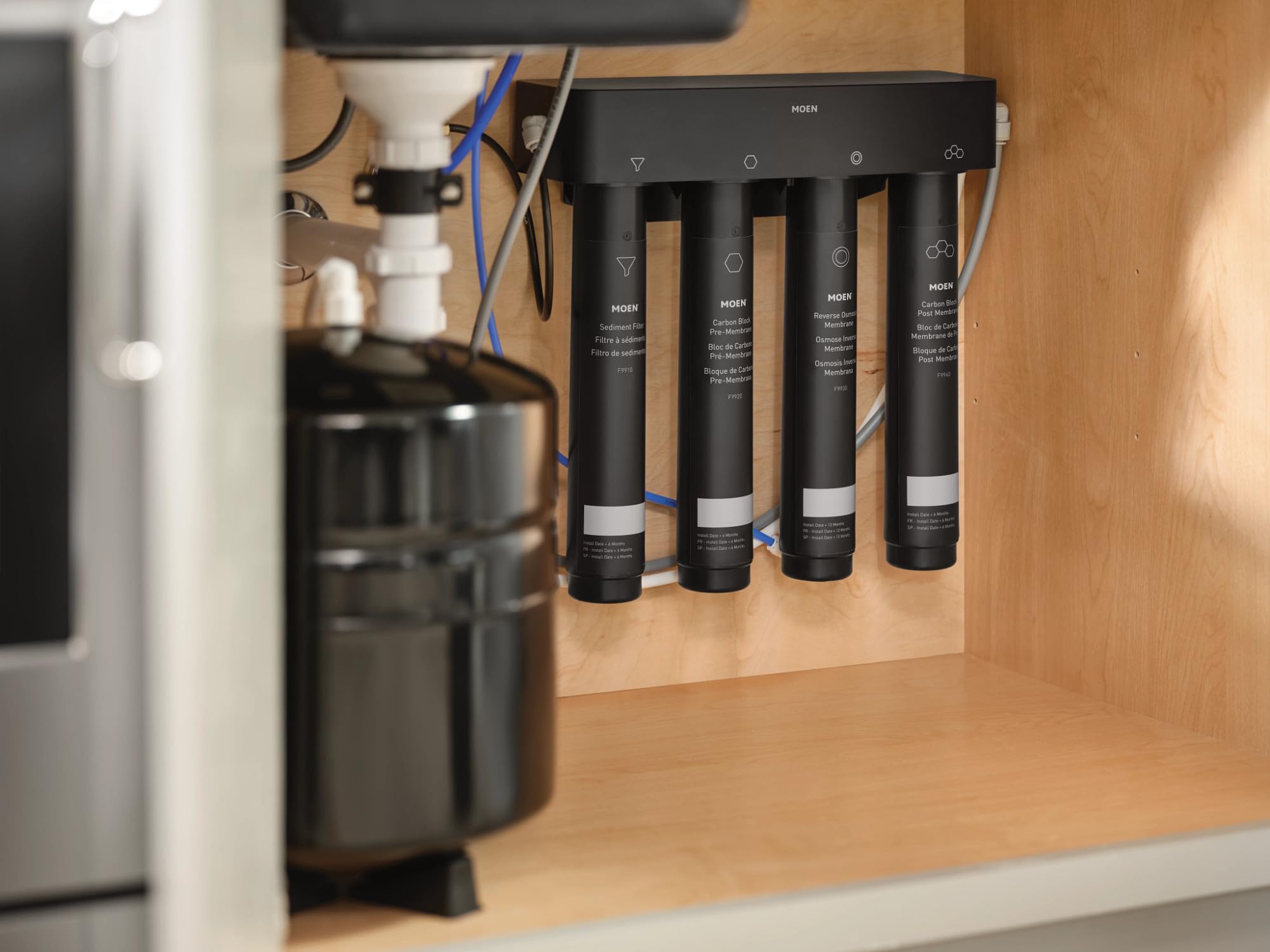 Moen 4-stage reverse osmosis filtration system installed under sink with four black filter cartridges and connected tubing.