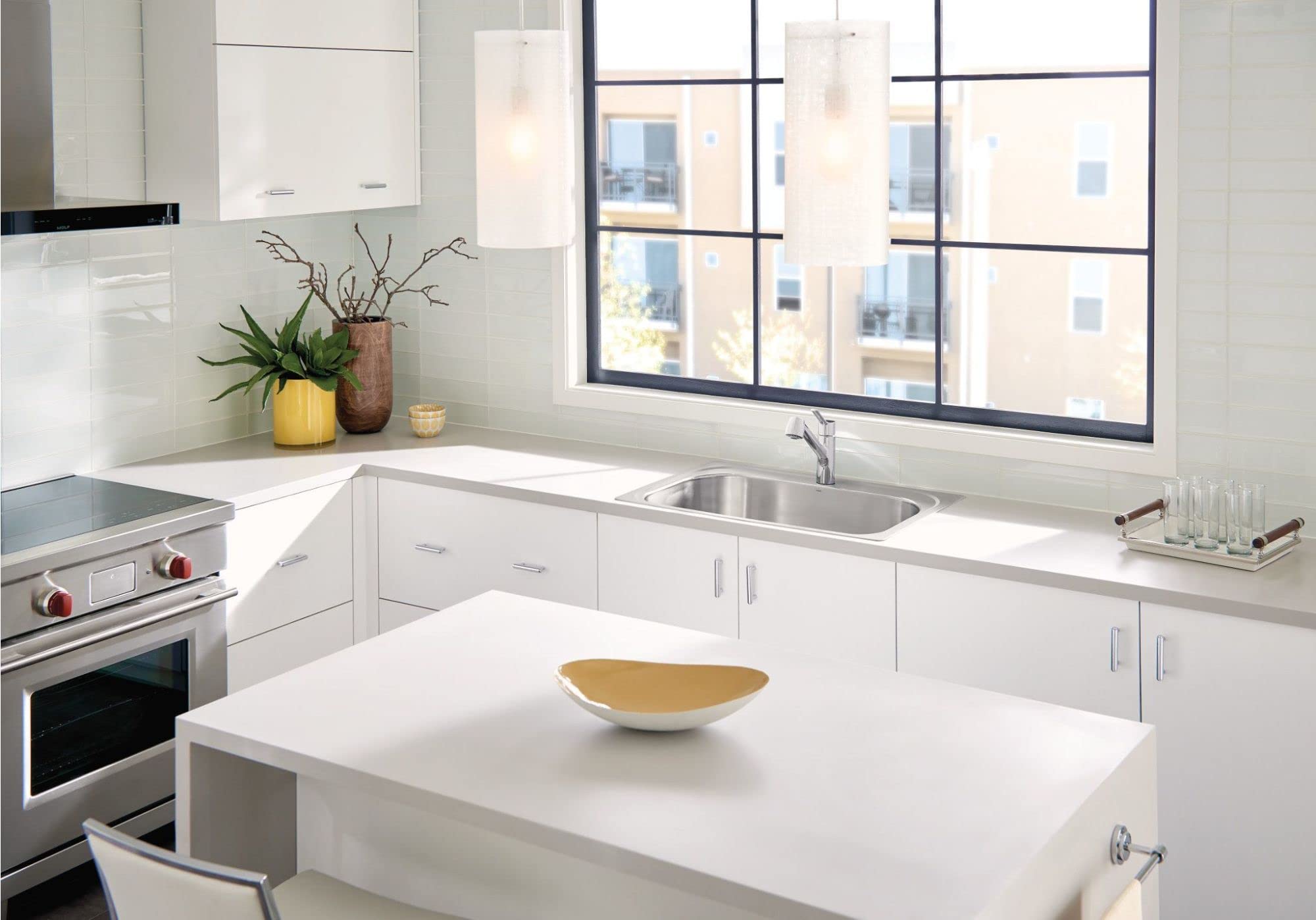Stainless steel single-handle kitchen faucet with pullout sprayer installed in white sink, shown in modern kitchen setting.