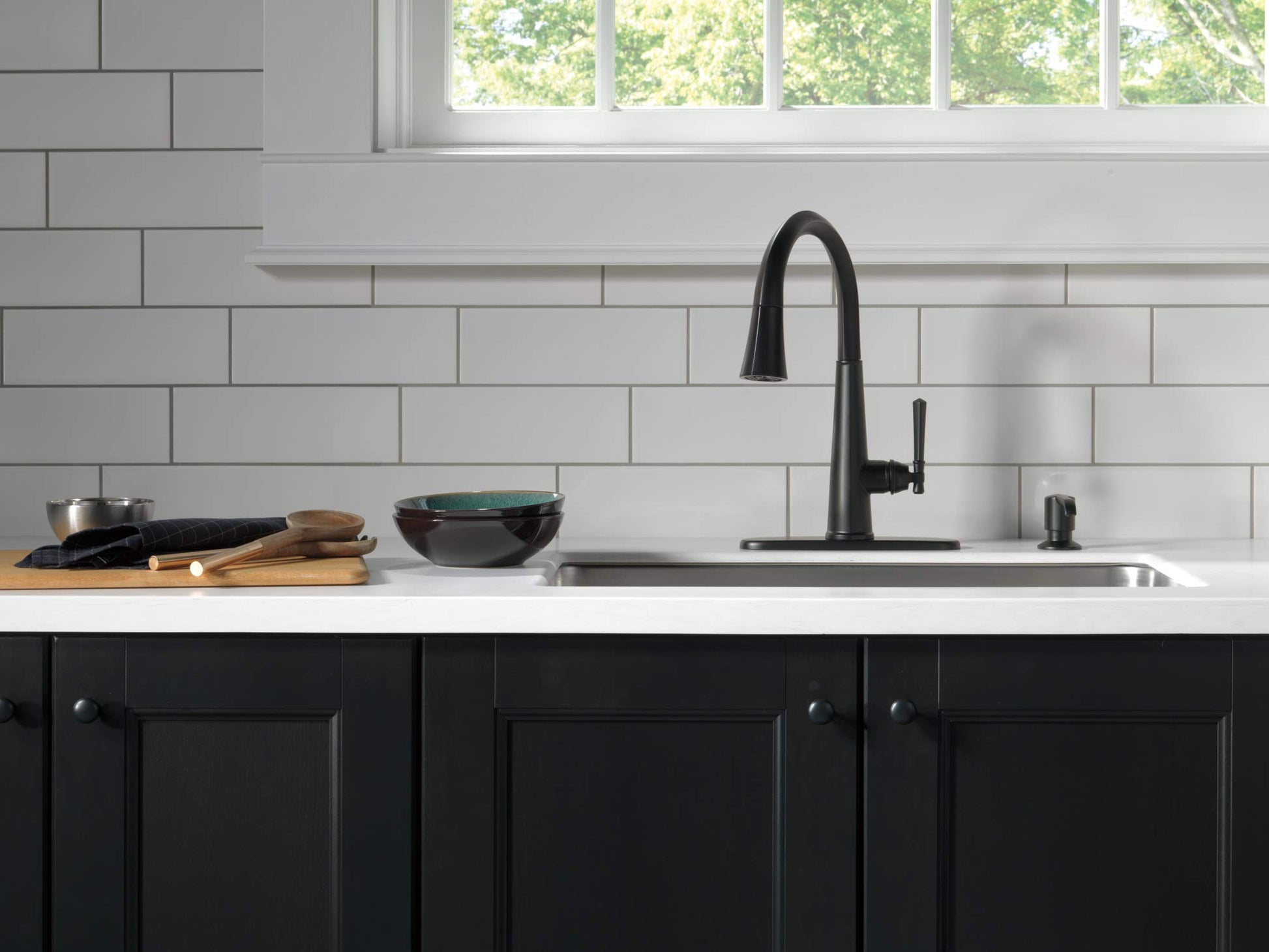 Matte black metal soap dispenser pump positioned on a white countertop next to a kitchen sink.