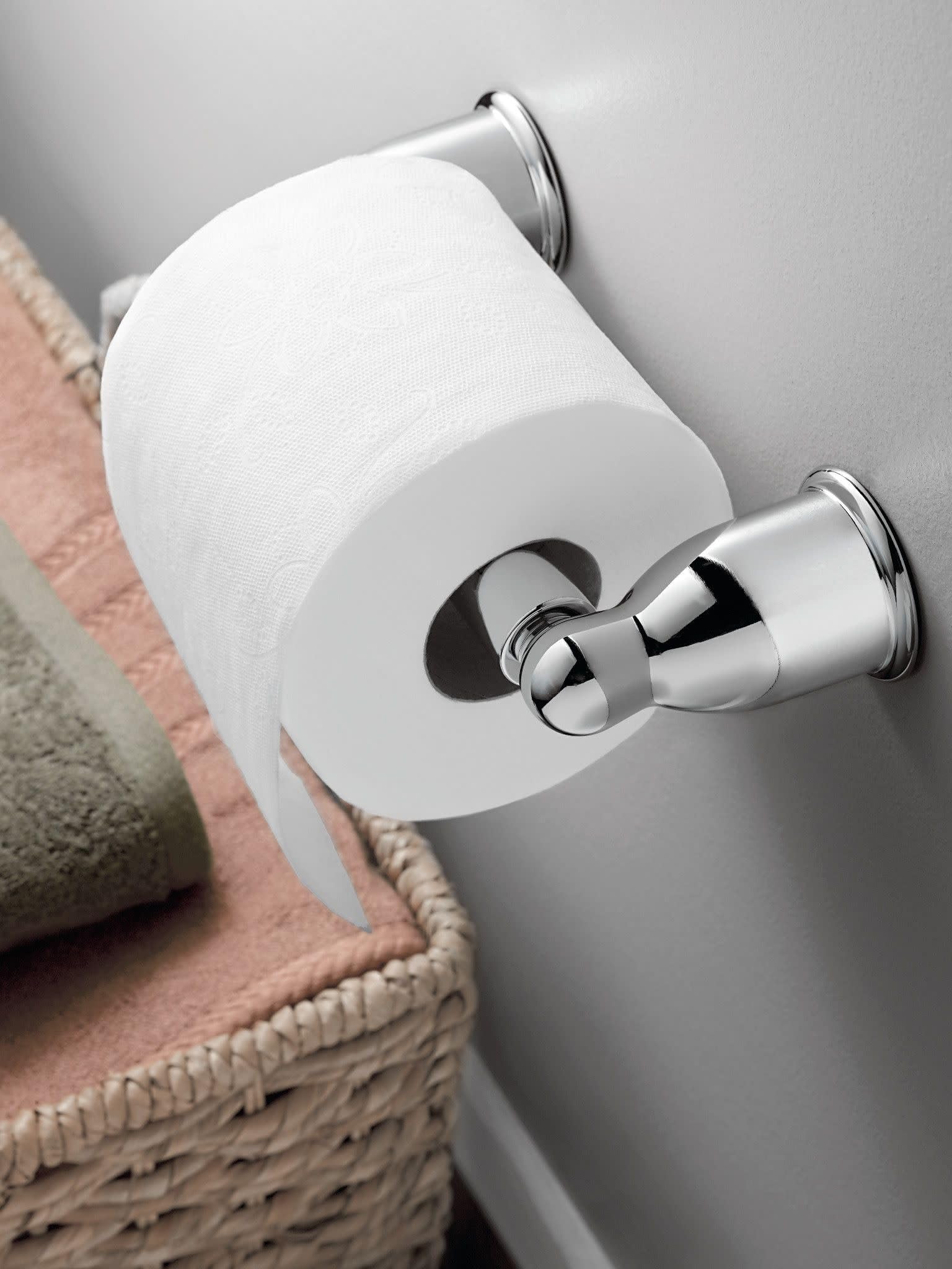 Chrome toilet paper holder mounted on wall with white toilet paper roll installed.