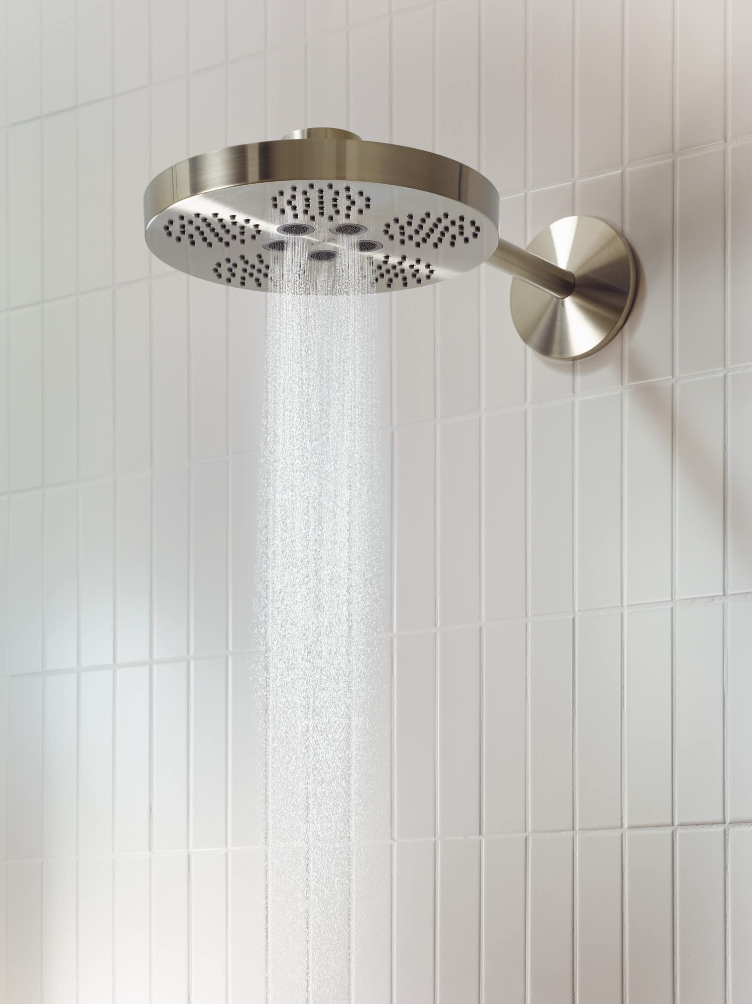 Brushed nickel round shower head with multiple spray jets mounted on wall with trim arm, dispensing water against white tiled