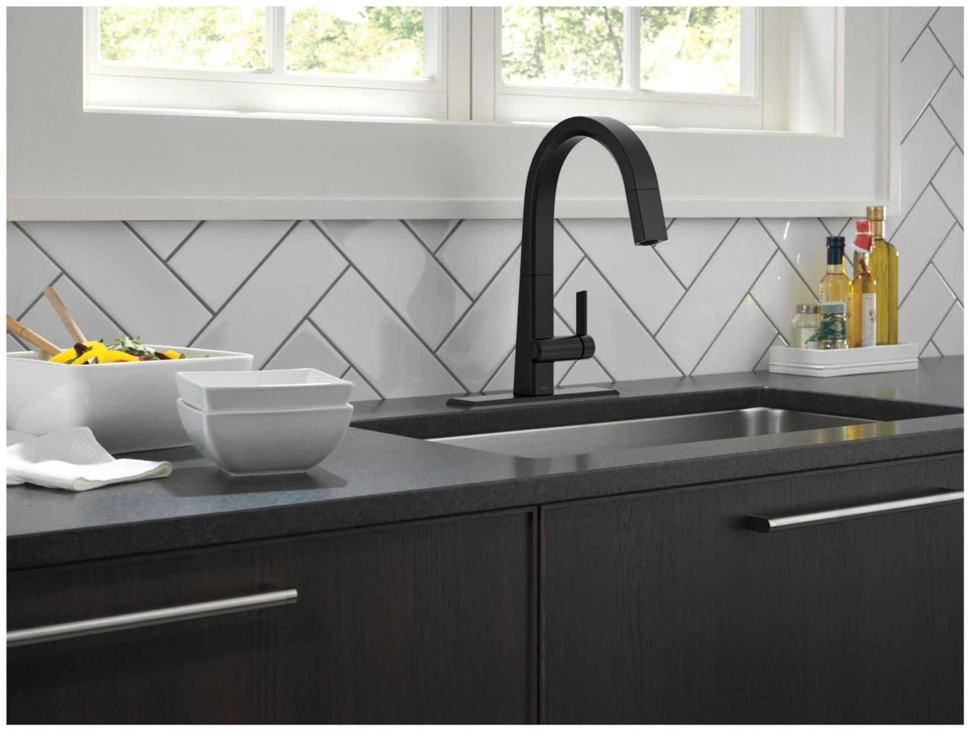 Black pull-down kitchen faucet with matching sink installed on black countertop in modern kitchen.