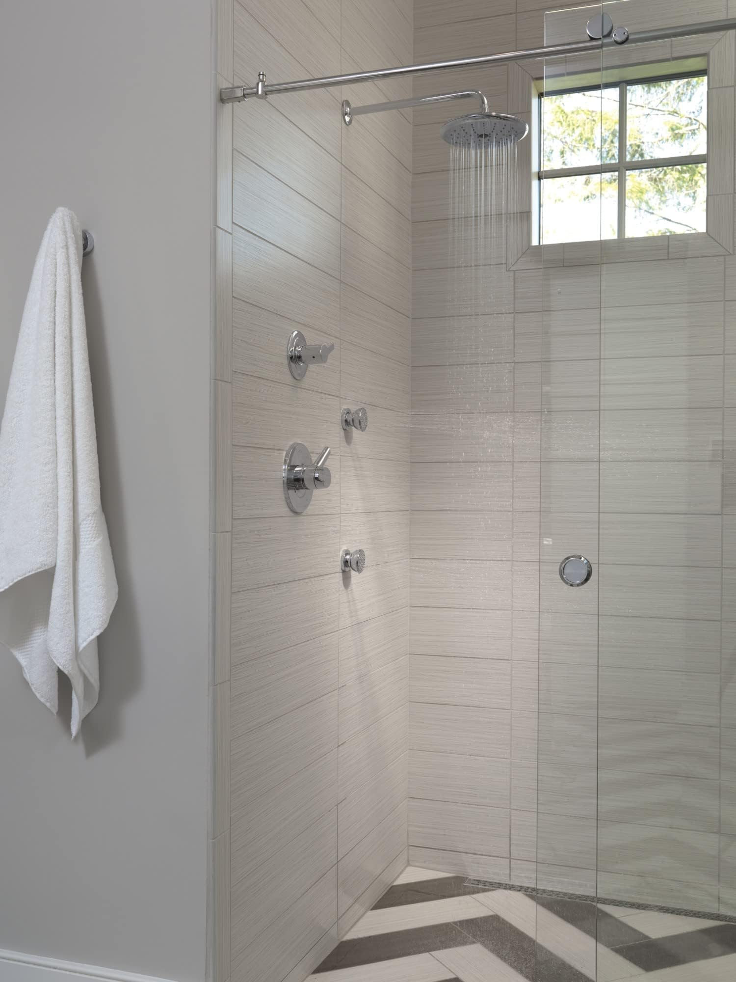 Polished nickel shower arm extending from ceiling to overhead rainfall showerhead in tiled bathroom.