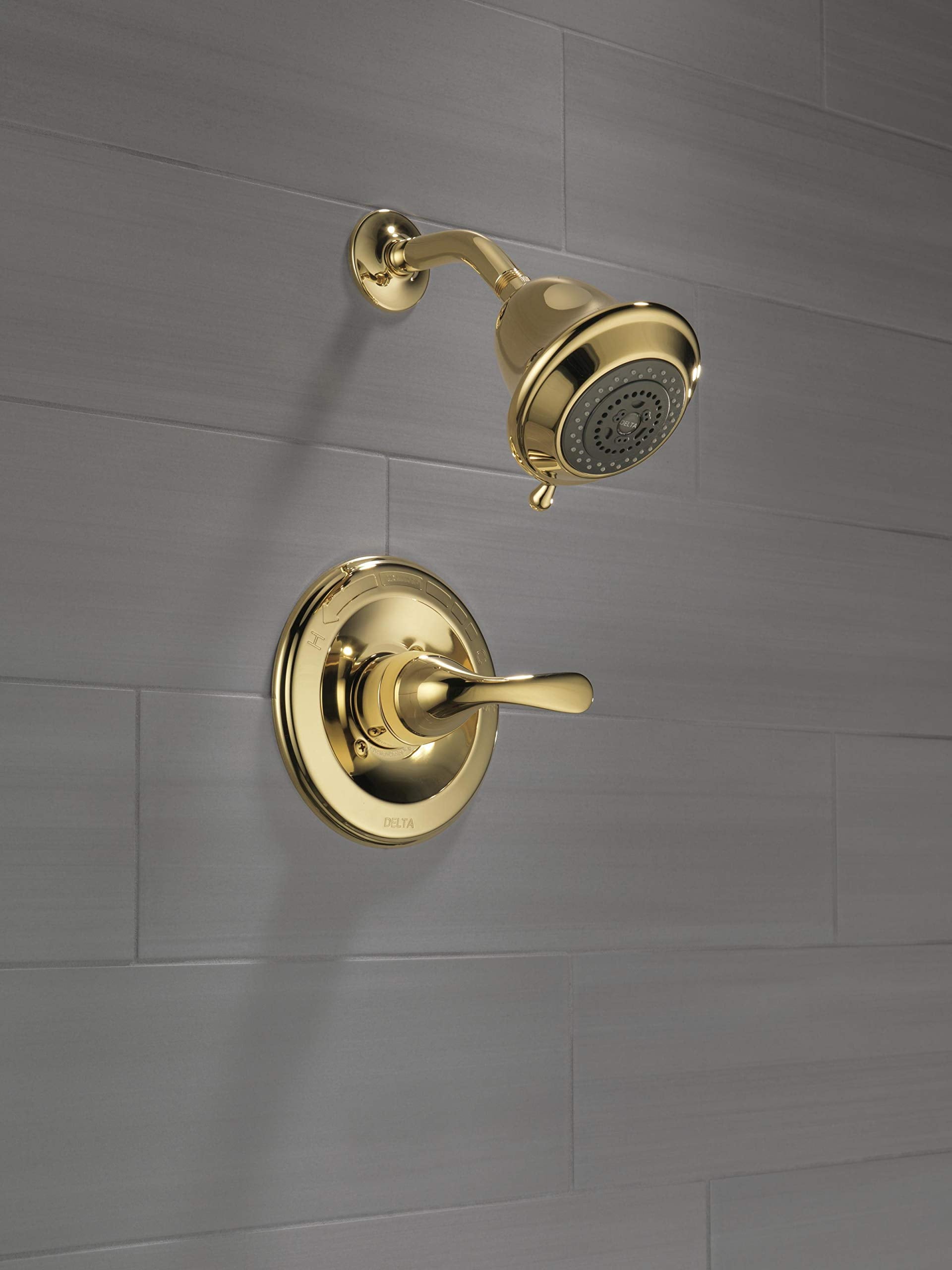 Polished brass shower trim with single lever handle and matching showerhead mounted on gray tile wall.