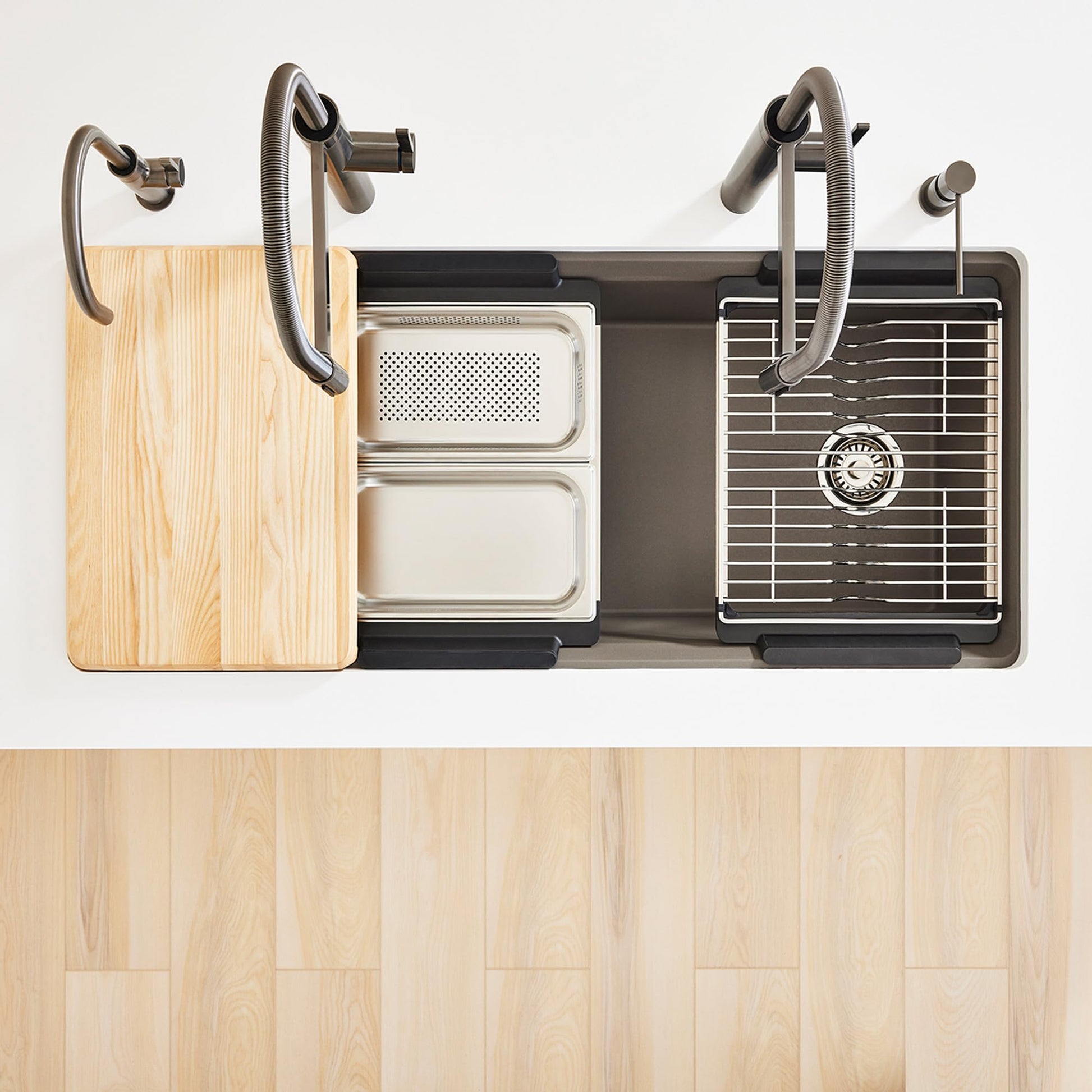 Stainless steel workstation sink organizer with wooden cutting board, perforated colander, grid rack, and flexible spray arms