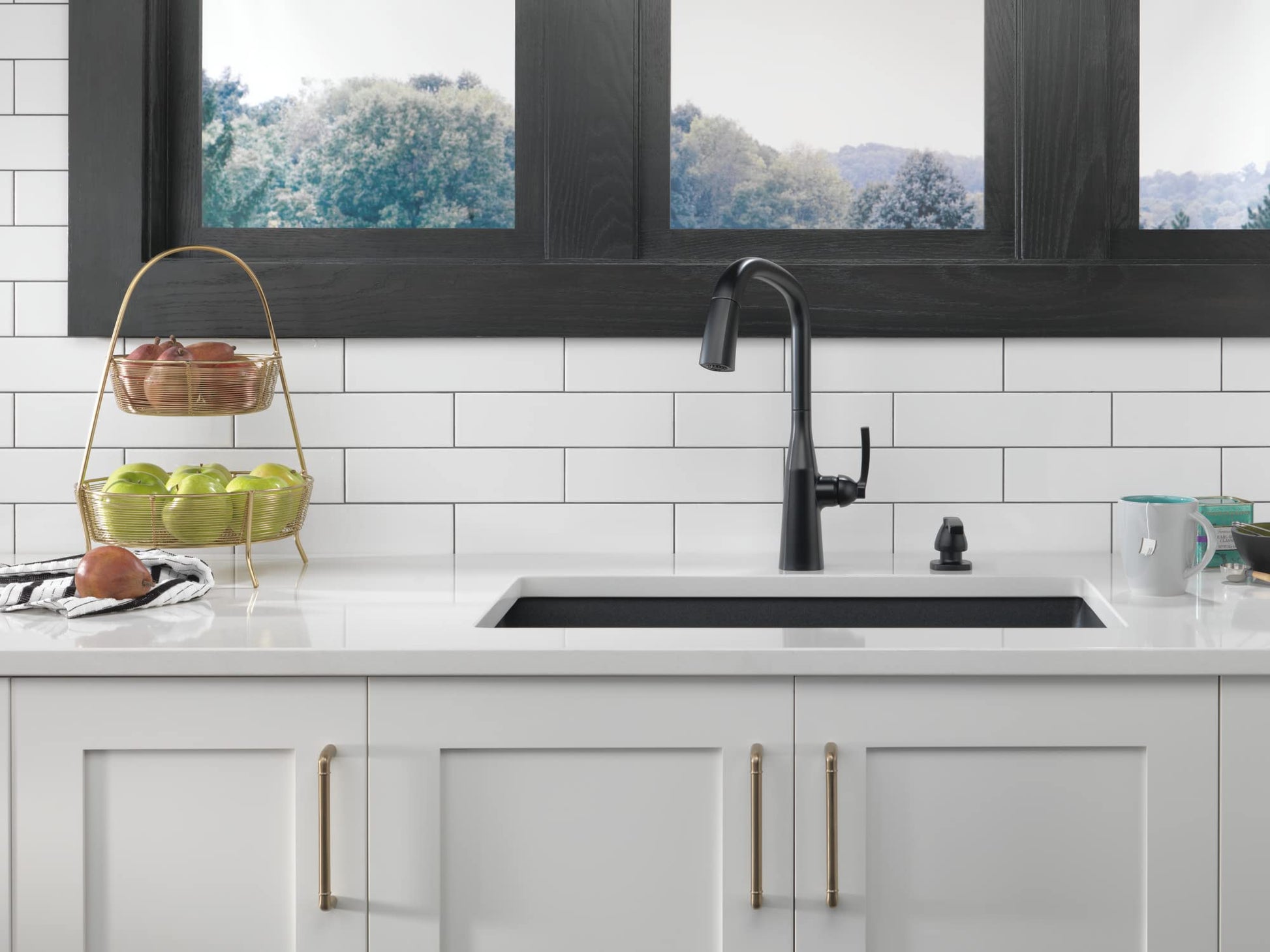 Matte black soap and lotion dispenser next to kitchen sink with pull-down faucet.
