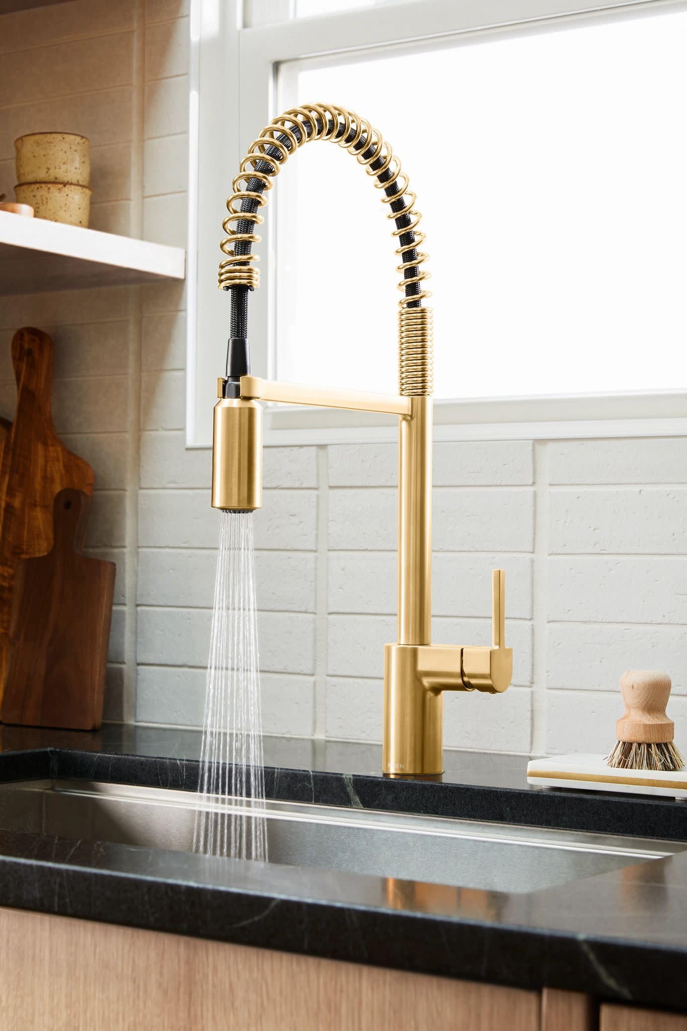 Brushed gold kitchen faucet with high arc spout, coiled pull-down hose, and single handle lever mounted on dark countertop.
