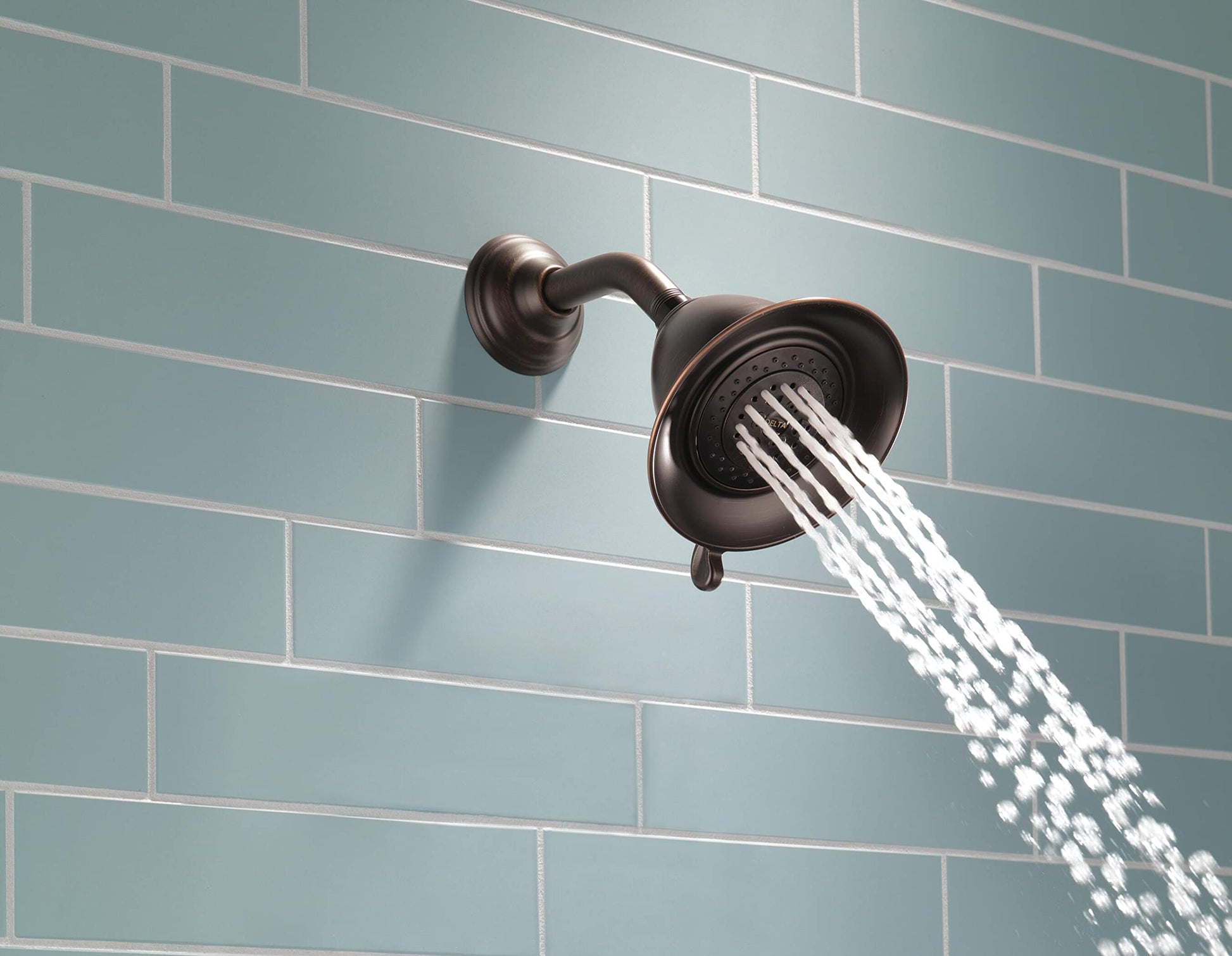 Chrome shower head with curved arm mount on tiled wall, water flowing downward in multiple streams.