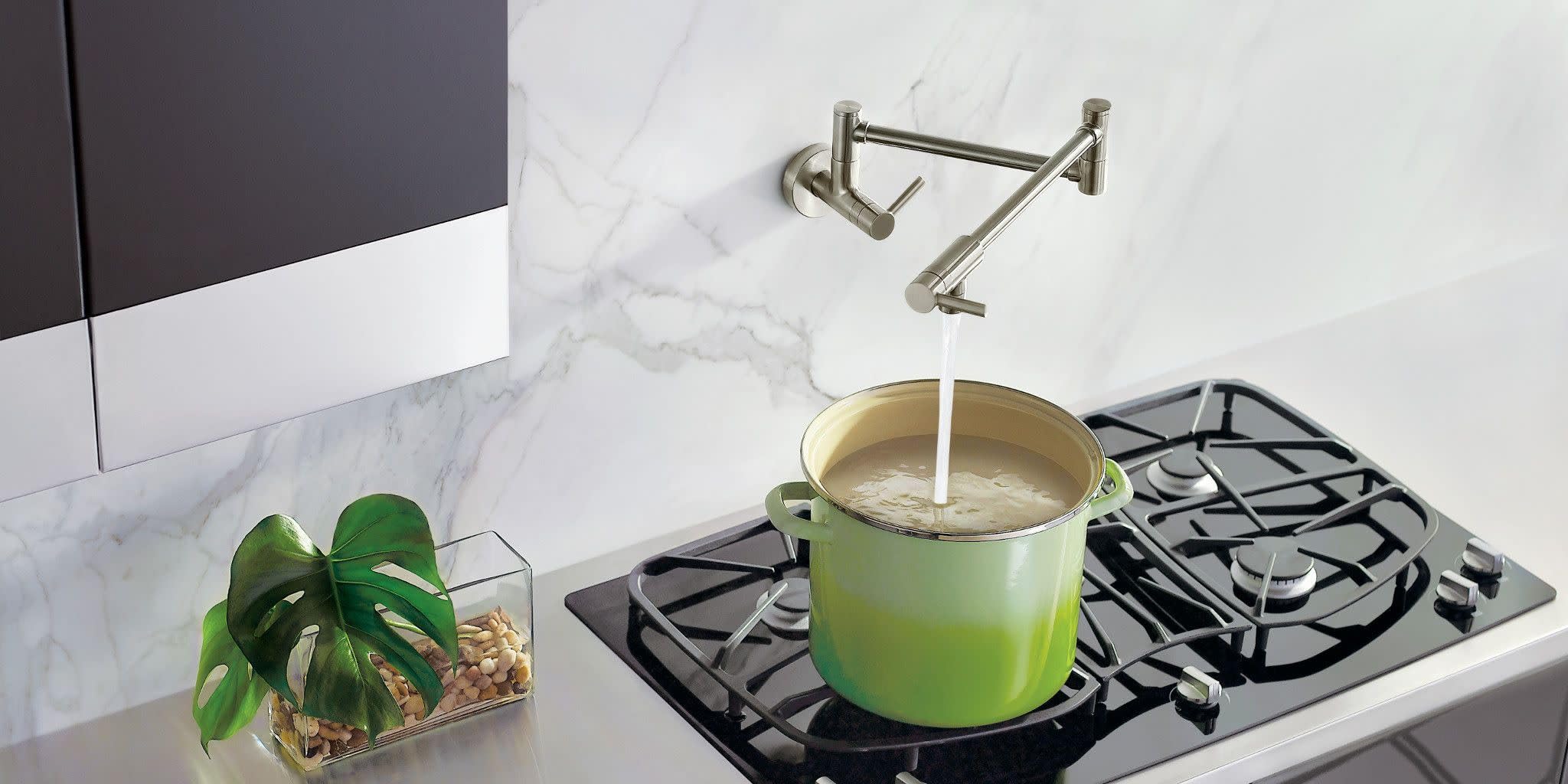 Stainless steel wall-mounted pot filler faucet with double-jointed swing arm positioned above green pot on stovetop.