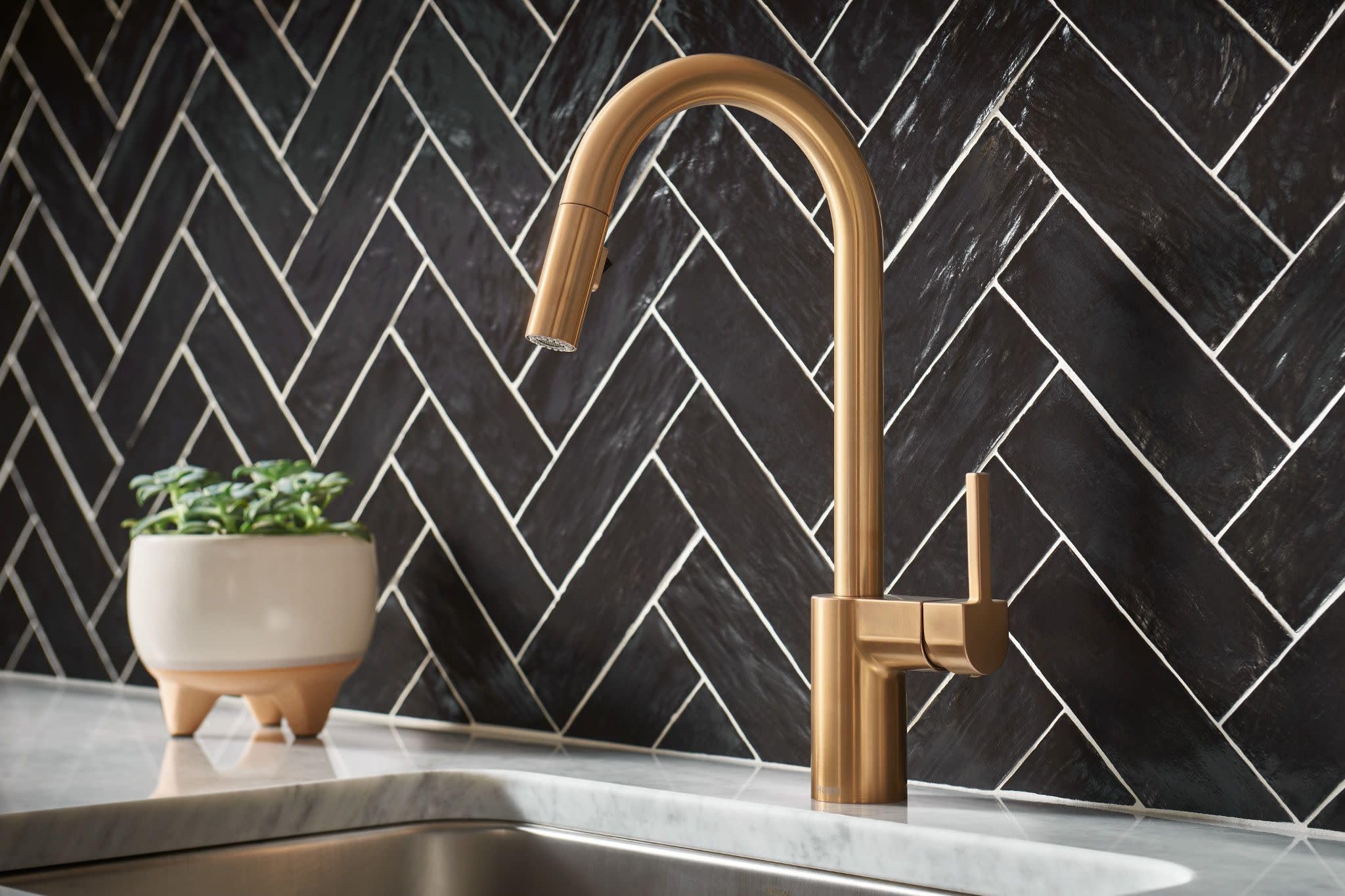 Brushed gold high-arc pulldown kitchen faucet with single handle mounted on white countertop against black herringbone tile b