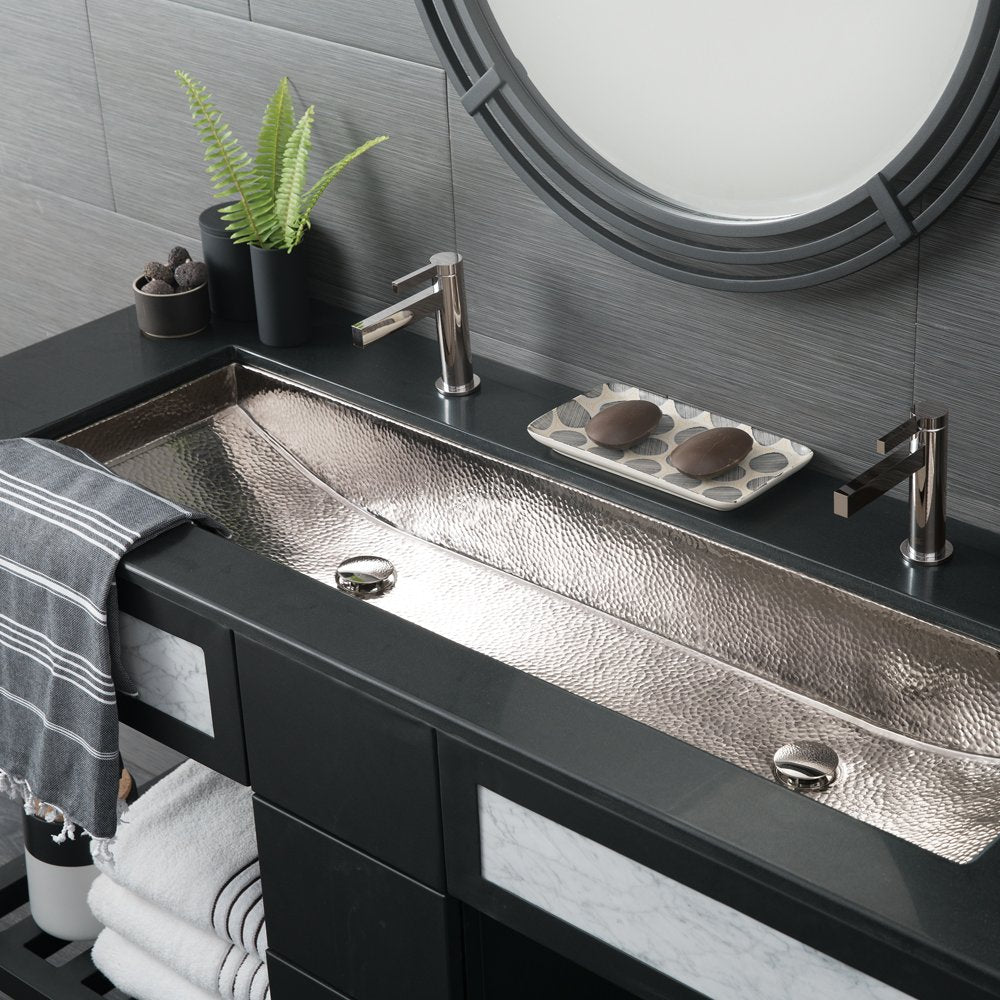 Polished nickel trough sink with hammered texture, dual faucets, and dual drains mounted on black vanity.