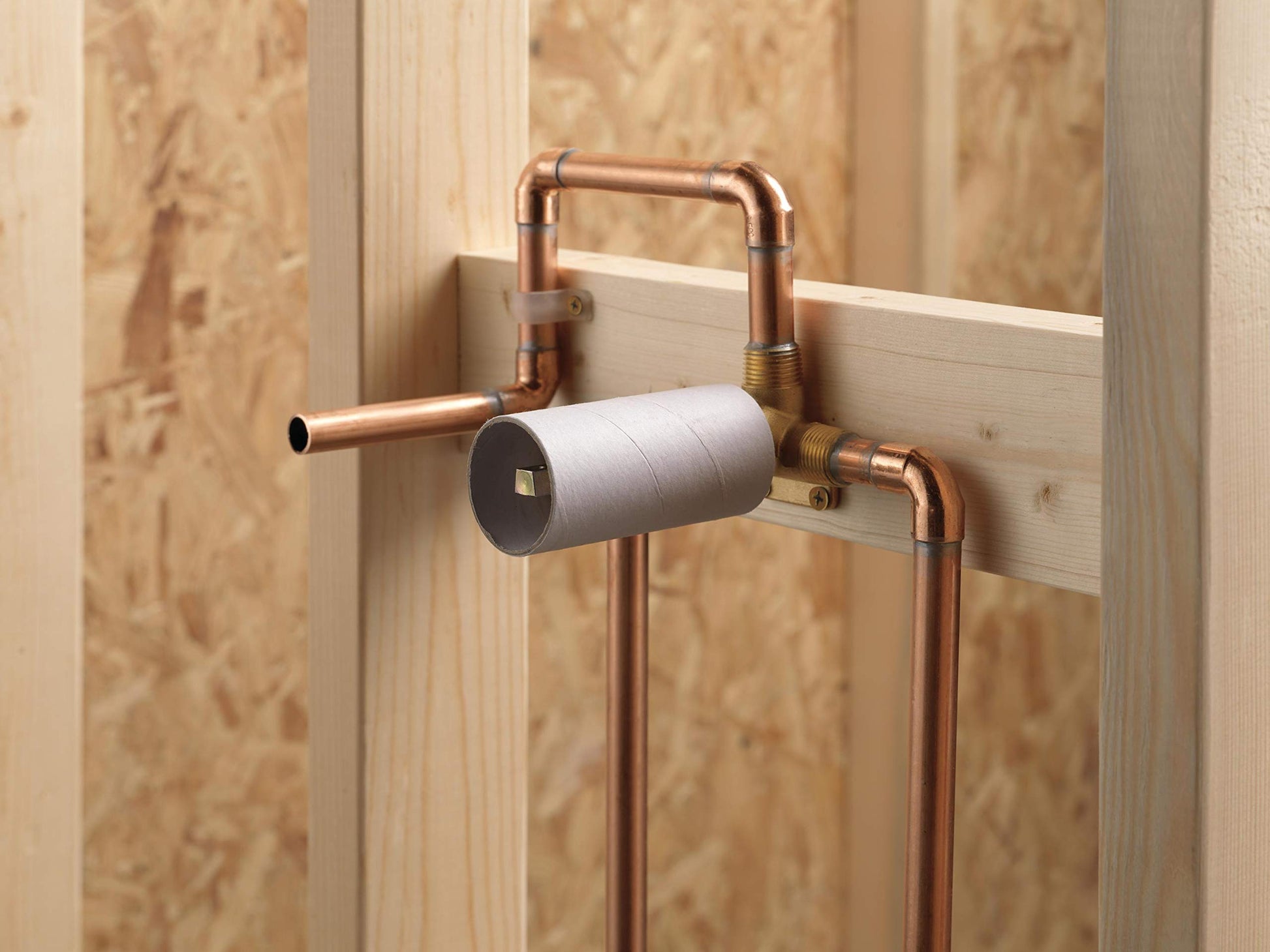 Copper wall-mounted single handle faucet rough-in with cylindrical handle and exposed plumbing pipes against wooden framing.