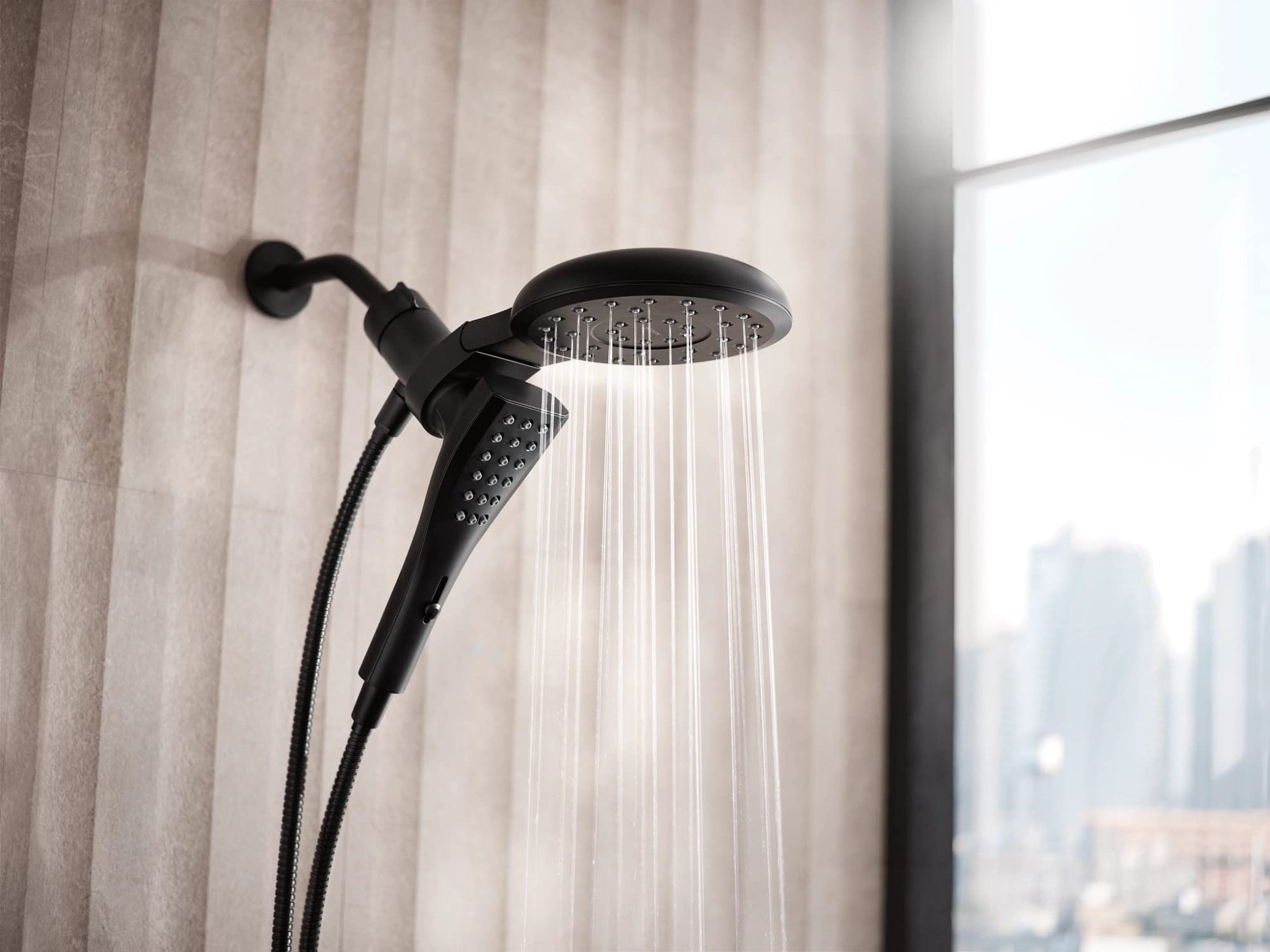 Matte black dual shower head system with handheld sprayer and overhead rainfall head mounted on bathroom wall.