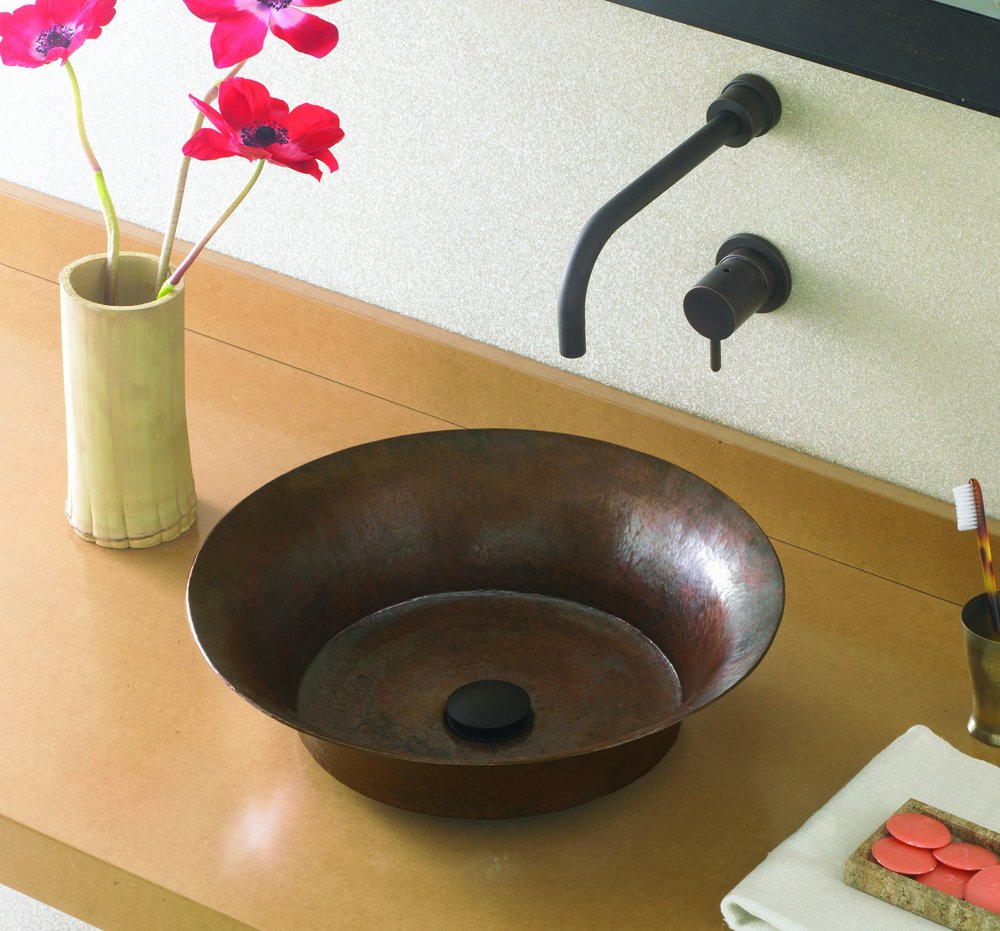 Antique copper vessel sink with curved walls and black wall-mounted faucet on countertop.