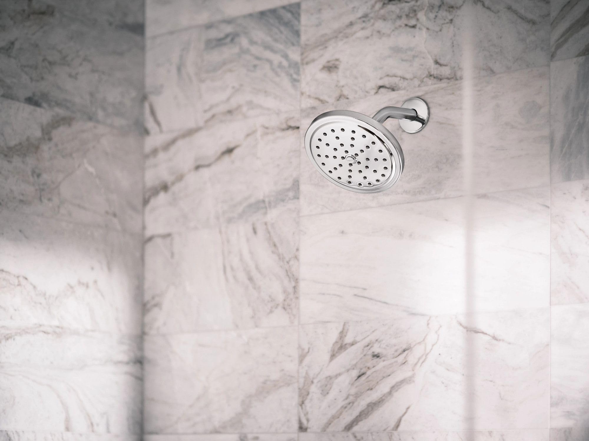 Chrome rainfall showerhead with perforated spray pattern mounted on marble tile wall.