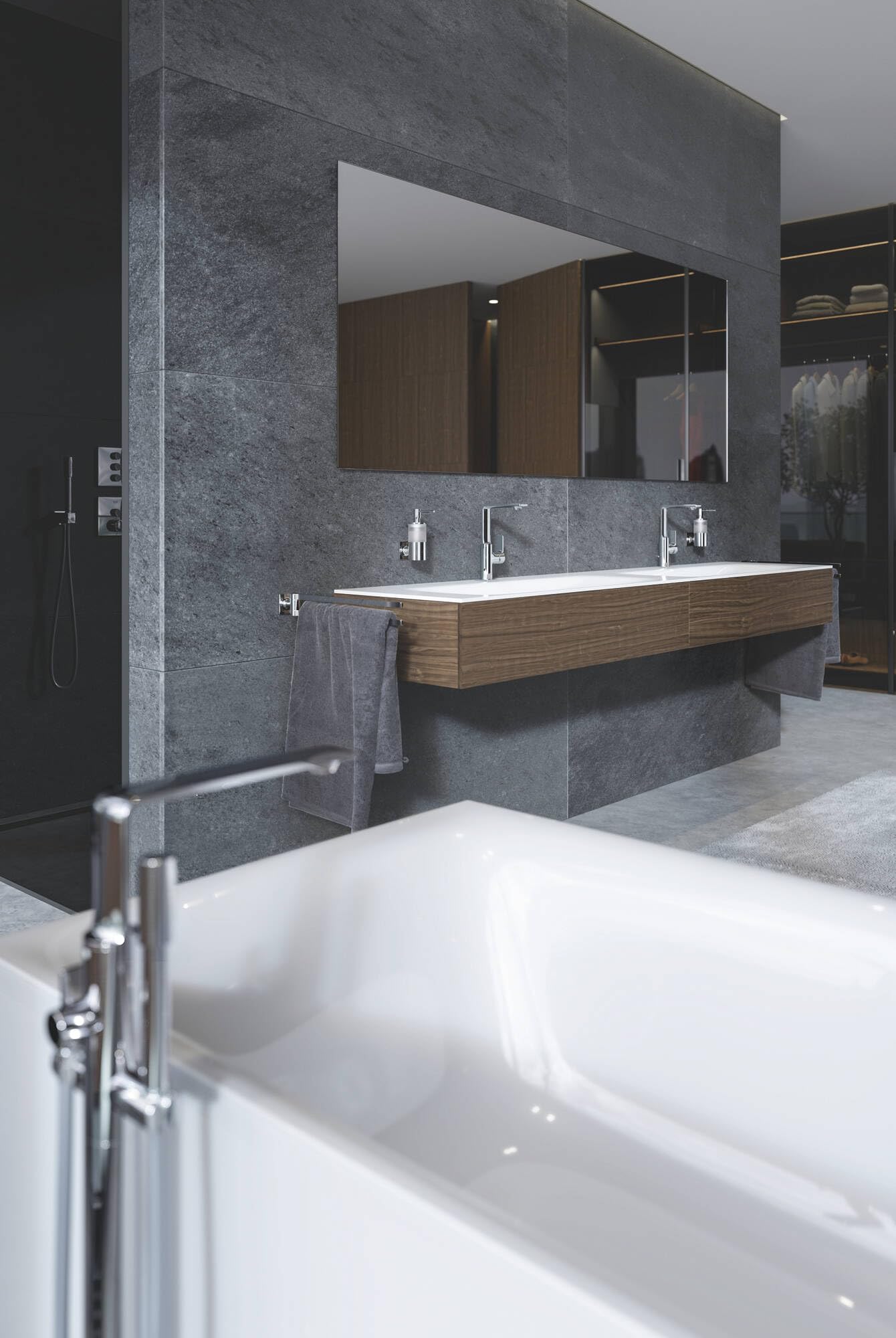 Chrome soap dispenser mounted on gray tile wall next to bathroom sink vanity.