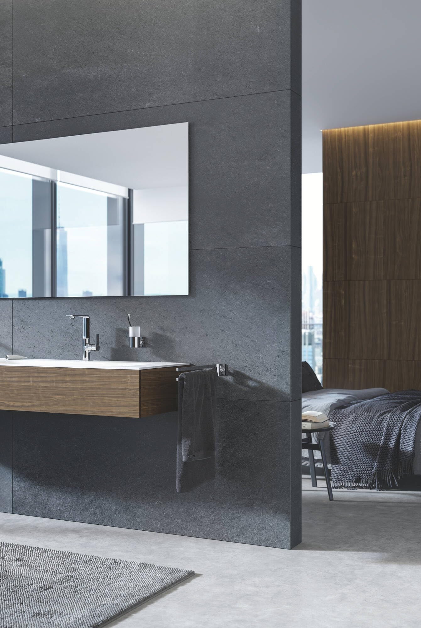 Chrome soap dispenser mounted on gray tile wall next to bathroom sink with faucet.