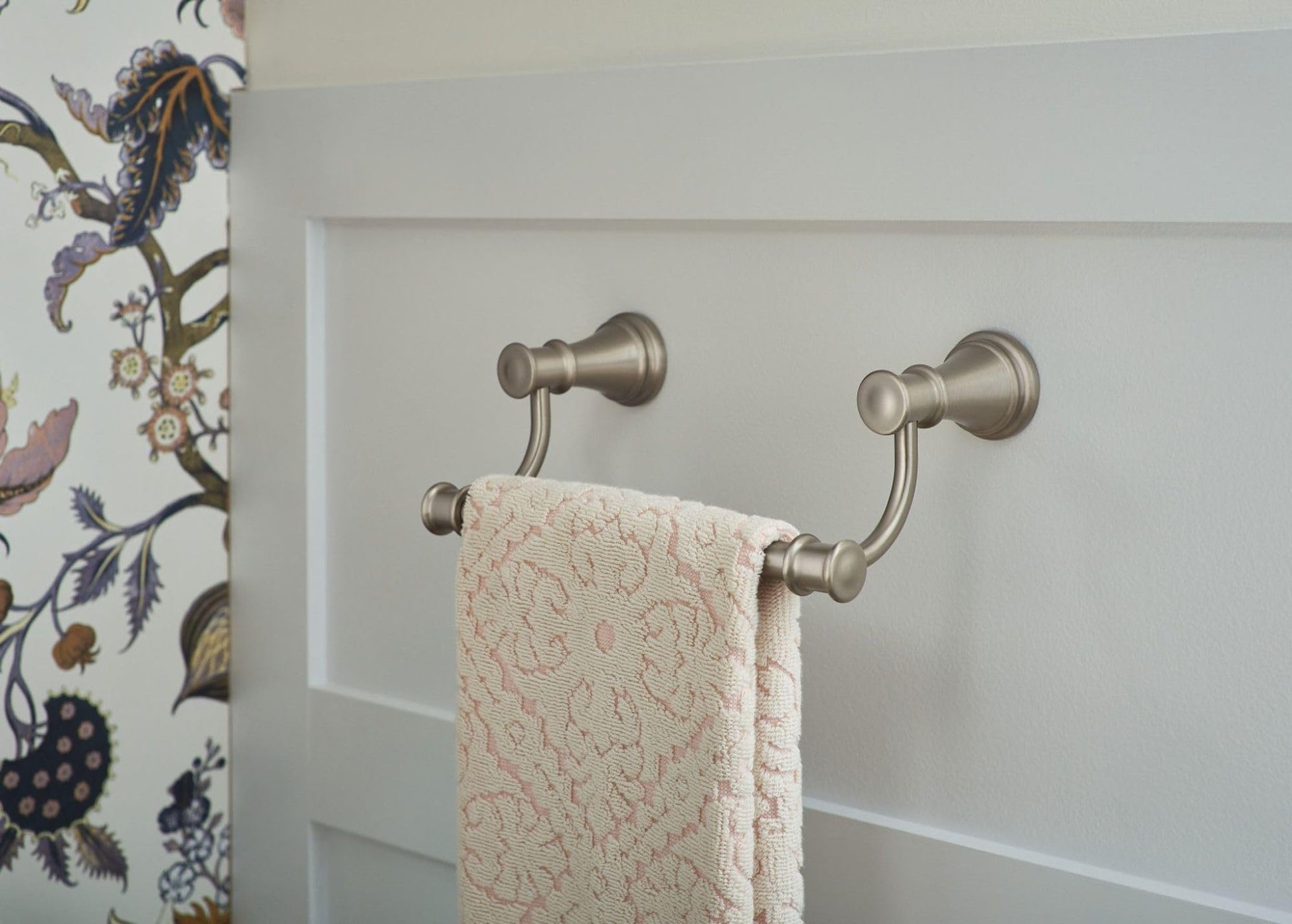 Brushed nickel double towel ring with two curved arms mounted on white wall, holding a cream-colored towel.