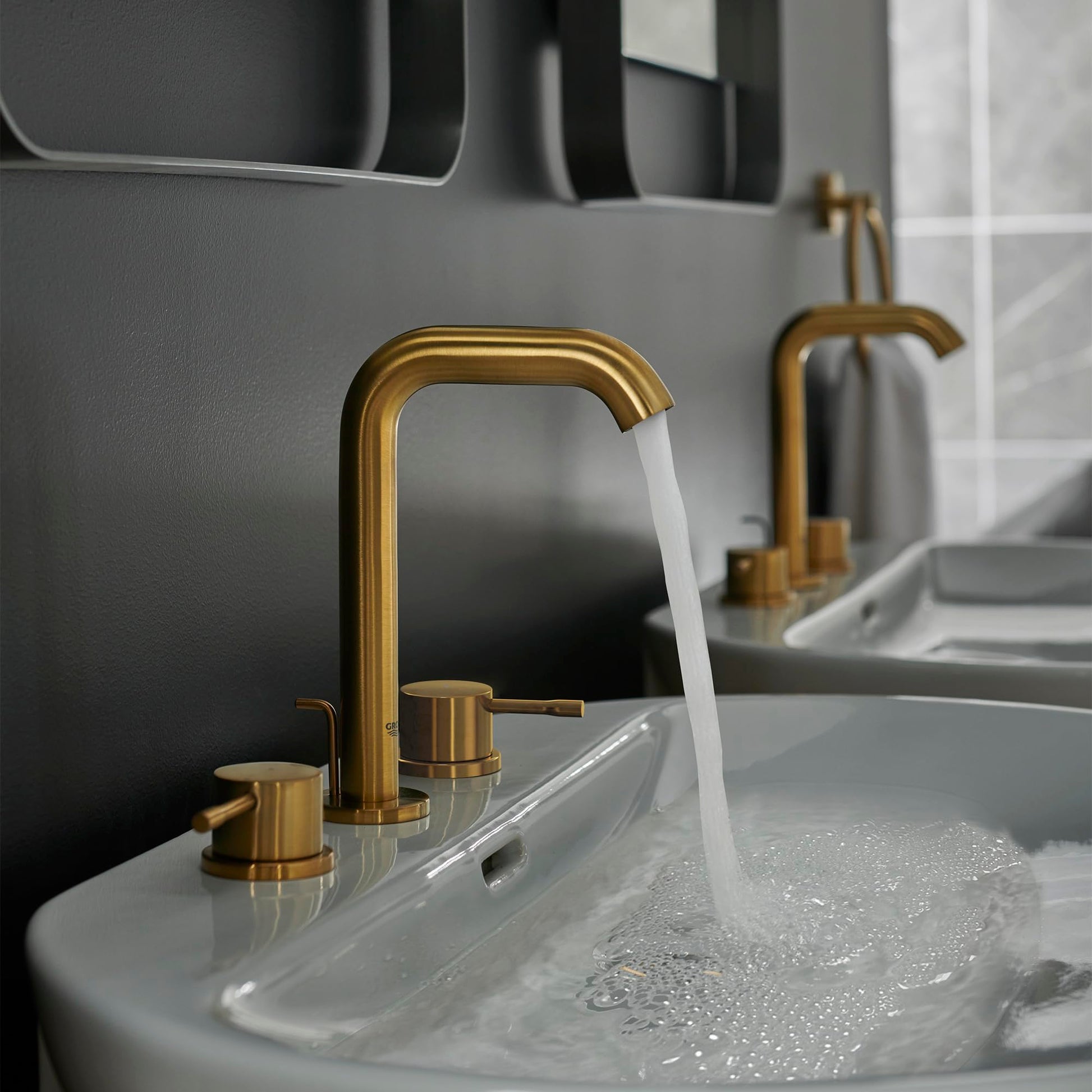 Grohe Essence widespread bathroom faucet with arched spout and two handles in brushed gold finish, shown installed on white s