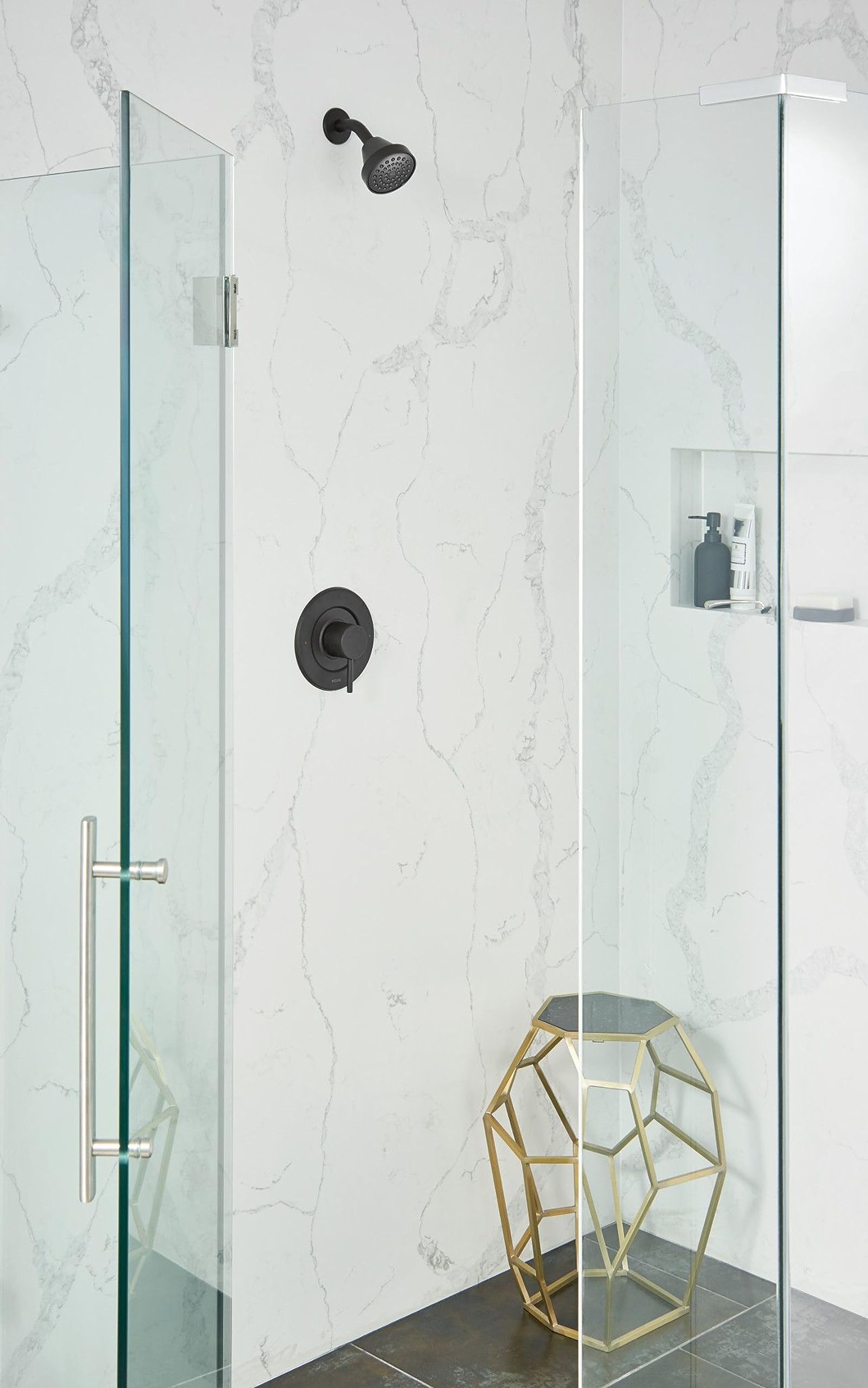 Matte black fixed showerhead with perforated face mounted on marble-tiled shower wall above valve control.