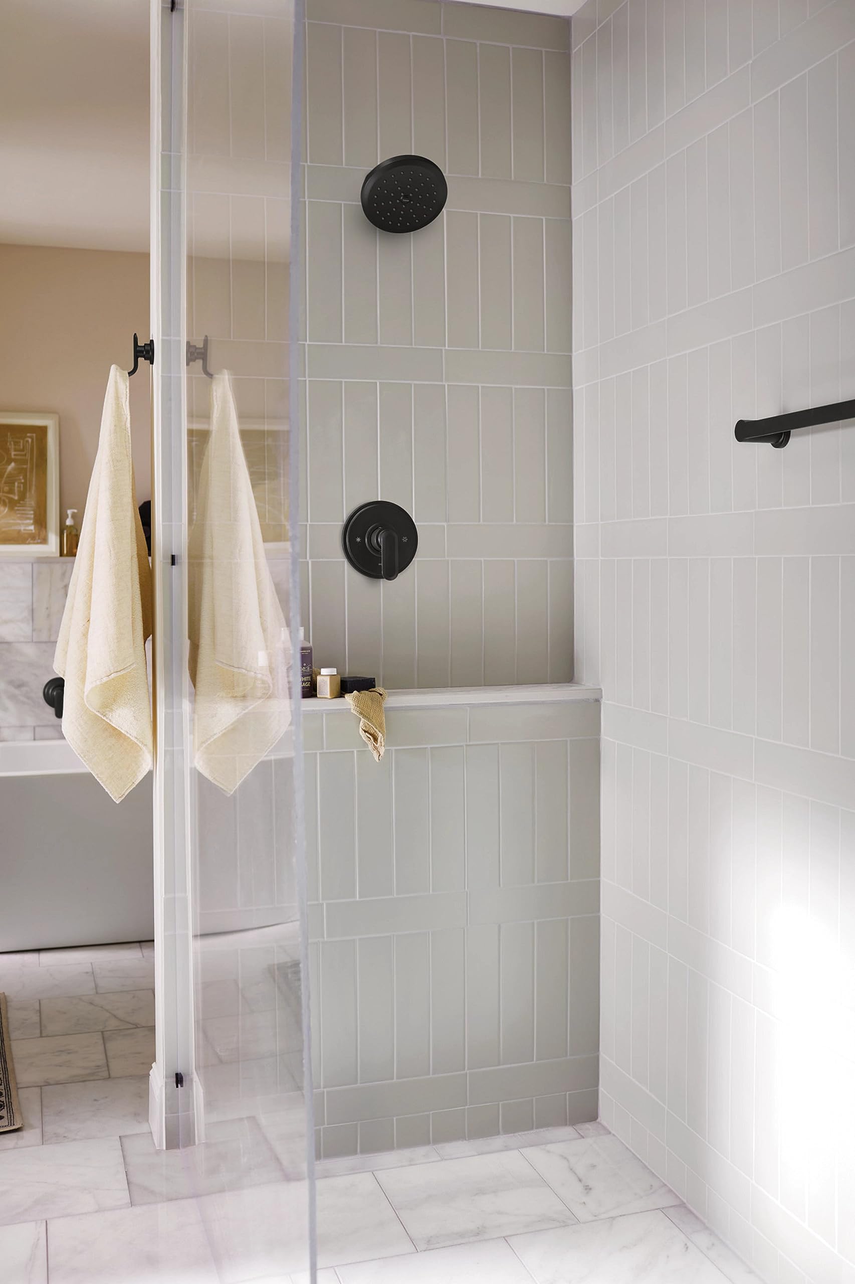 Matte black shower trim with round showerhead and lever handle mounted on white subway tile shower wall.