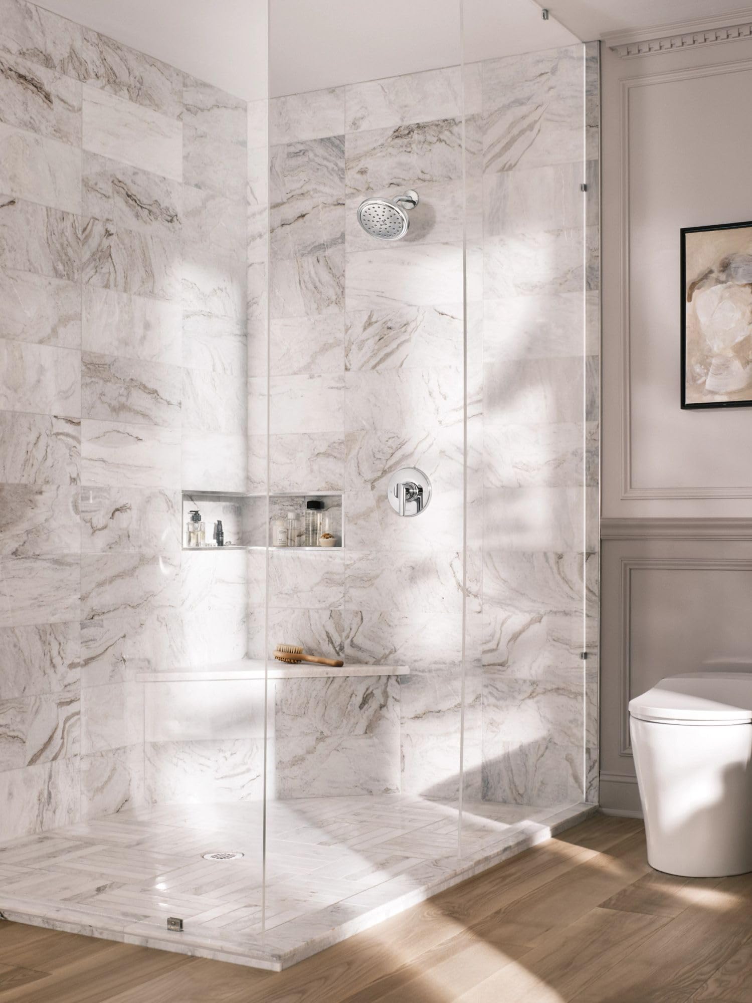 Chrome single-handle shower trim with round showerhead and control valve mounted on marble tile wall.