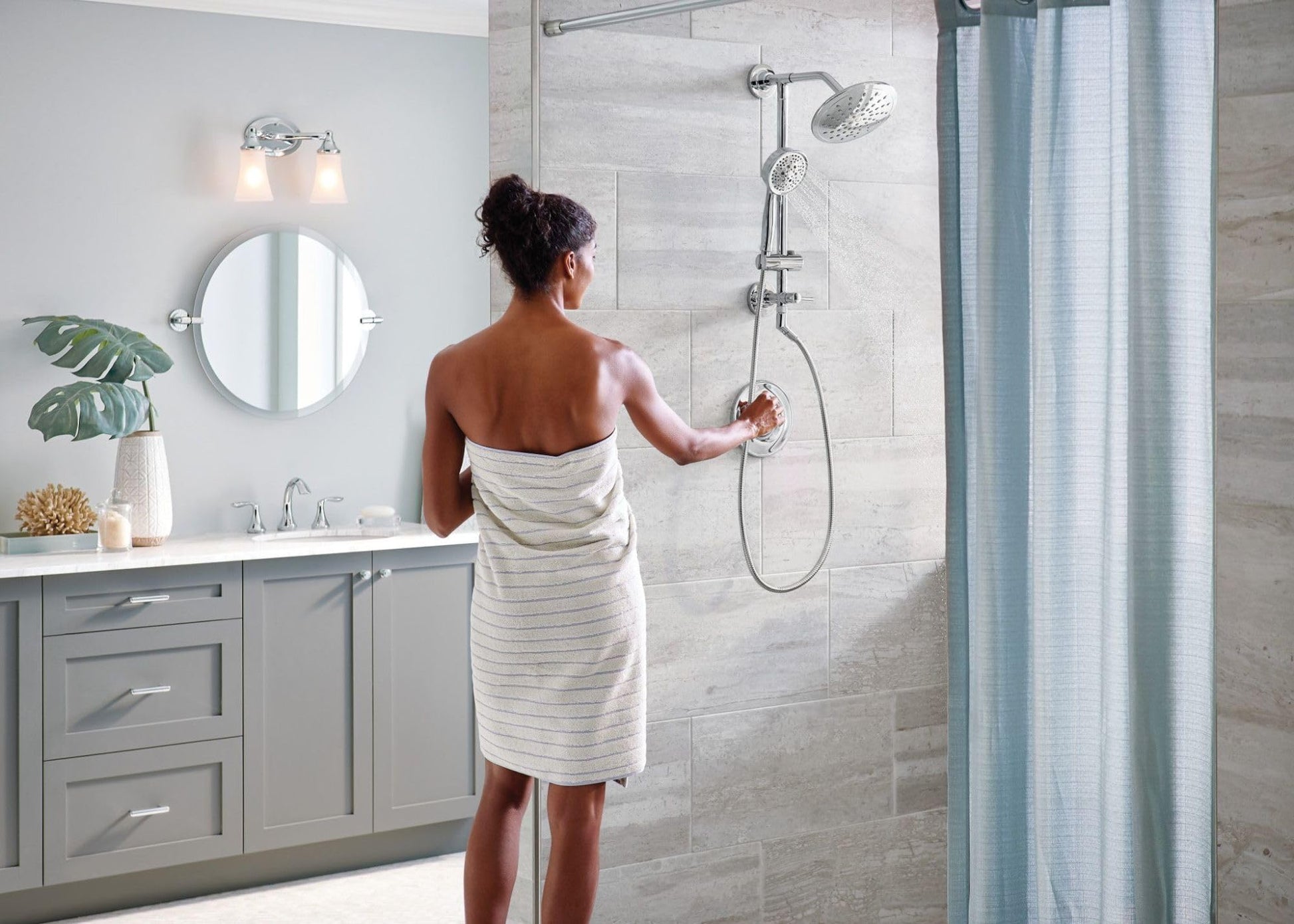 Chrome shower system with round rainshower head and handheld wand mounted on tile wall.