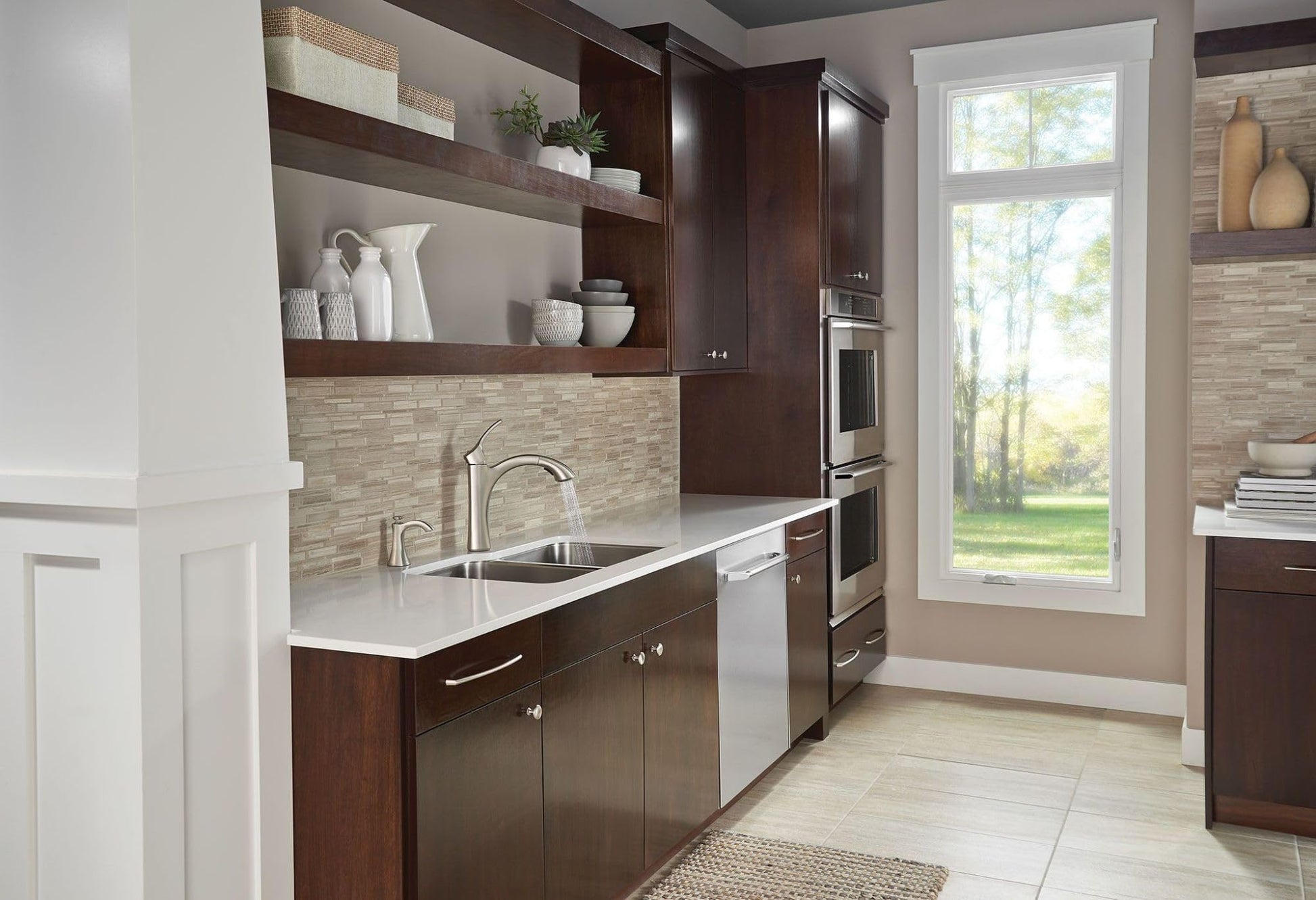 Stainless steel deck-mounted soap dispenser with pump positioned on kitchen counter next to sink.