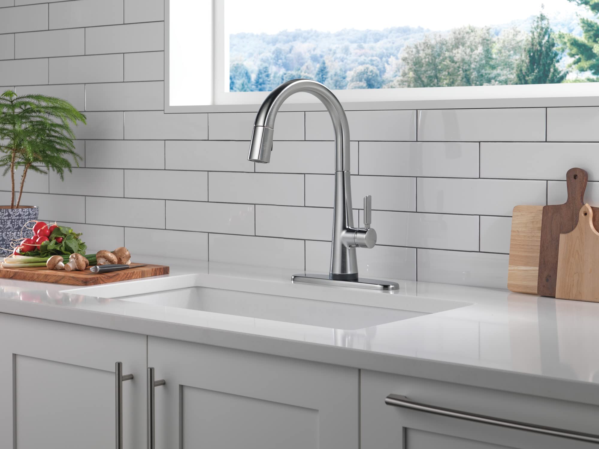 Stainless steel pull-down kitchen faucet with Arctic finish mounted above white sink in subway tile backsplash.