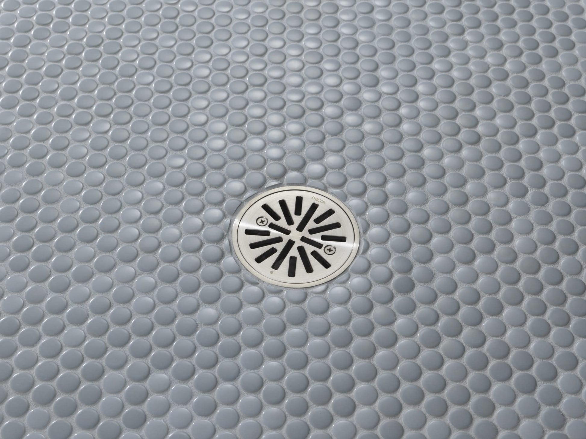 Stainless steel round shower drain with radial slot design installed in gray penny tile flooring.