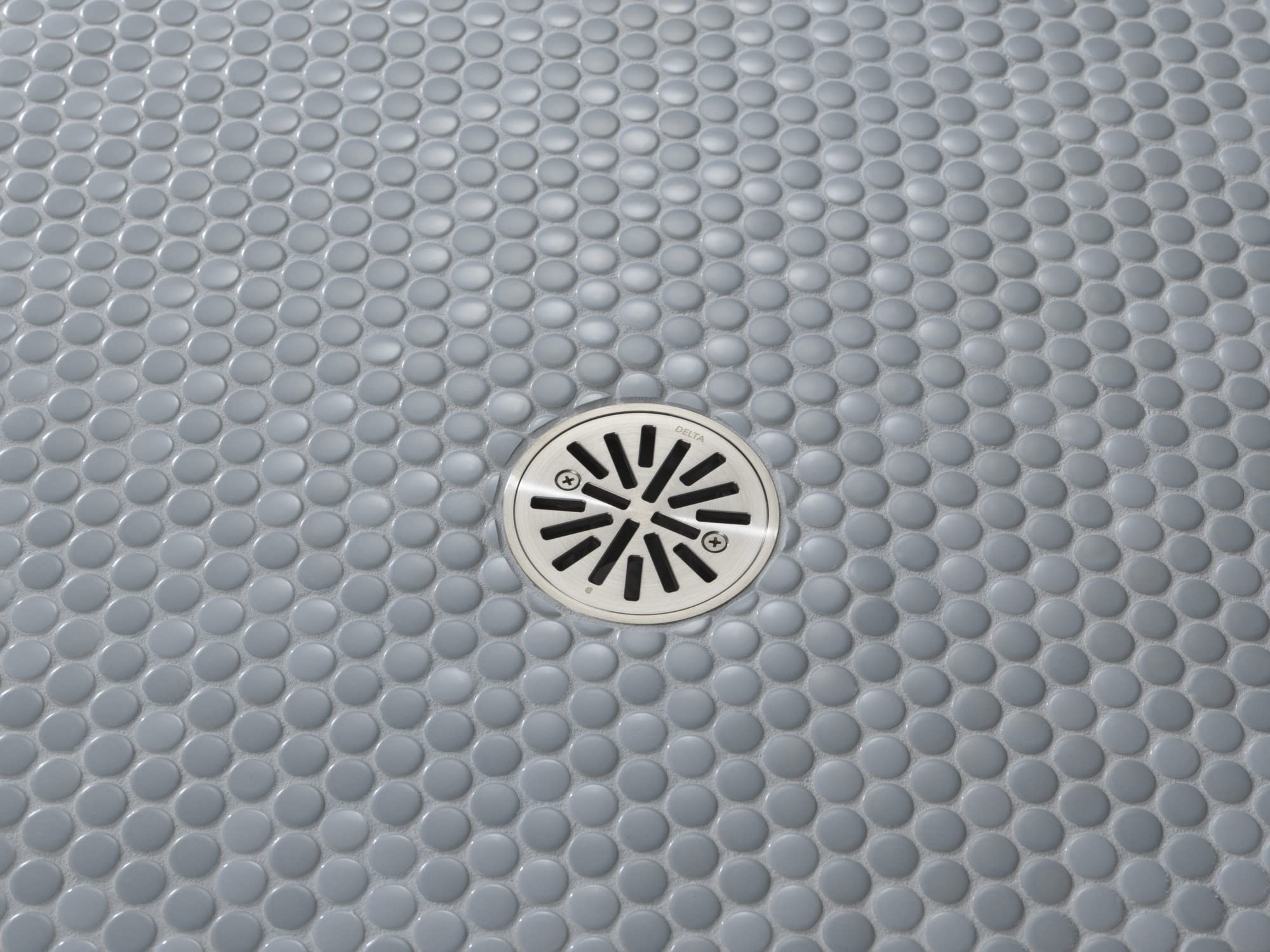 Stainless steel round shower drain with radial slot design installed in gray penny tile flooring.