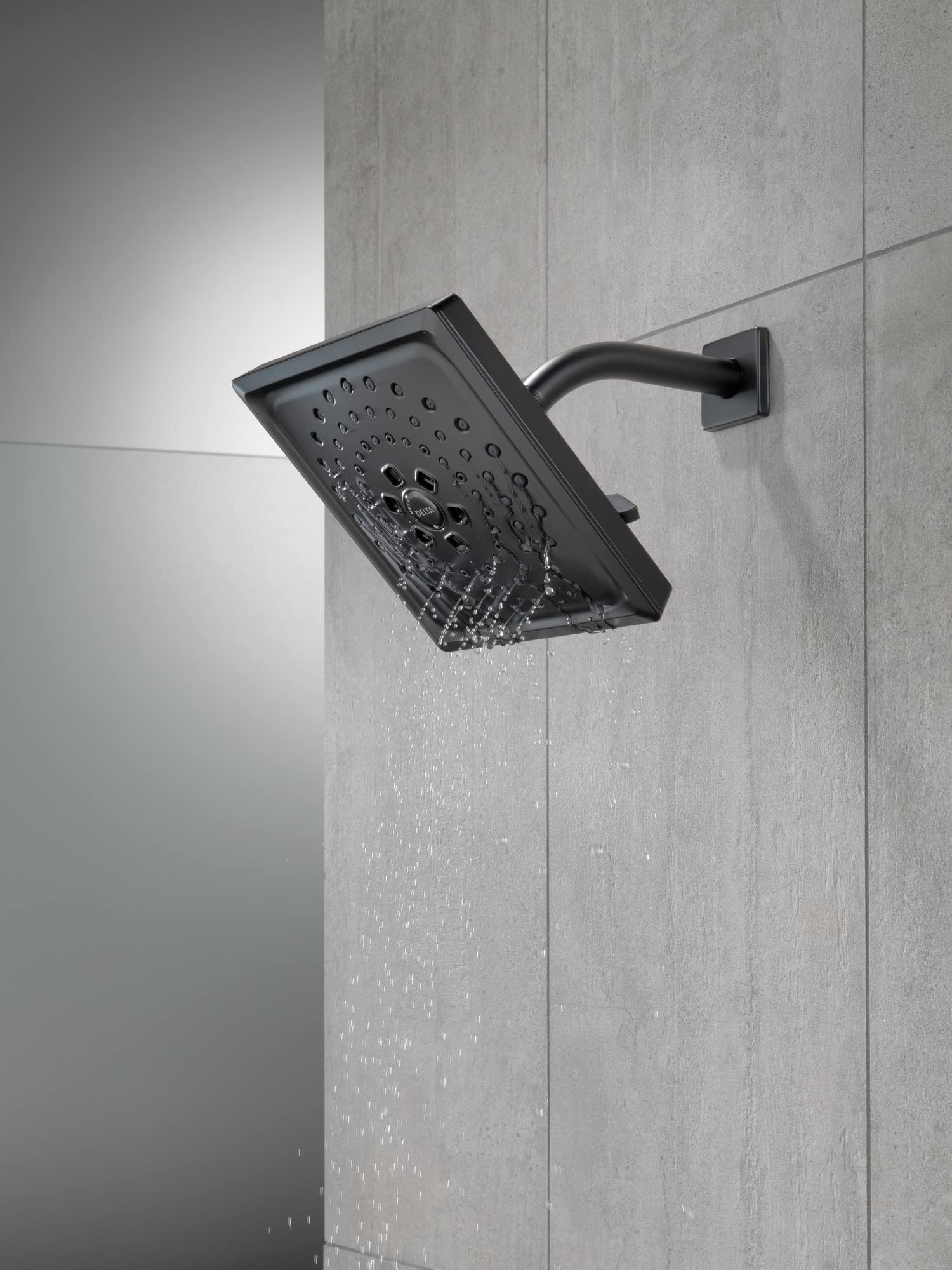 Matte black shower arm with square showerhead mounted on tile wall, water flowing from spray nozzles.