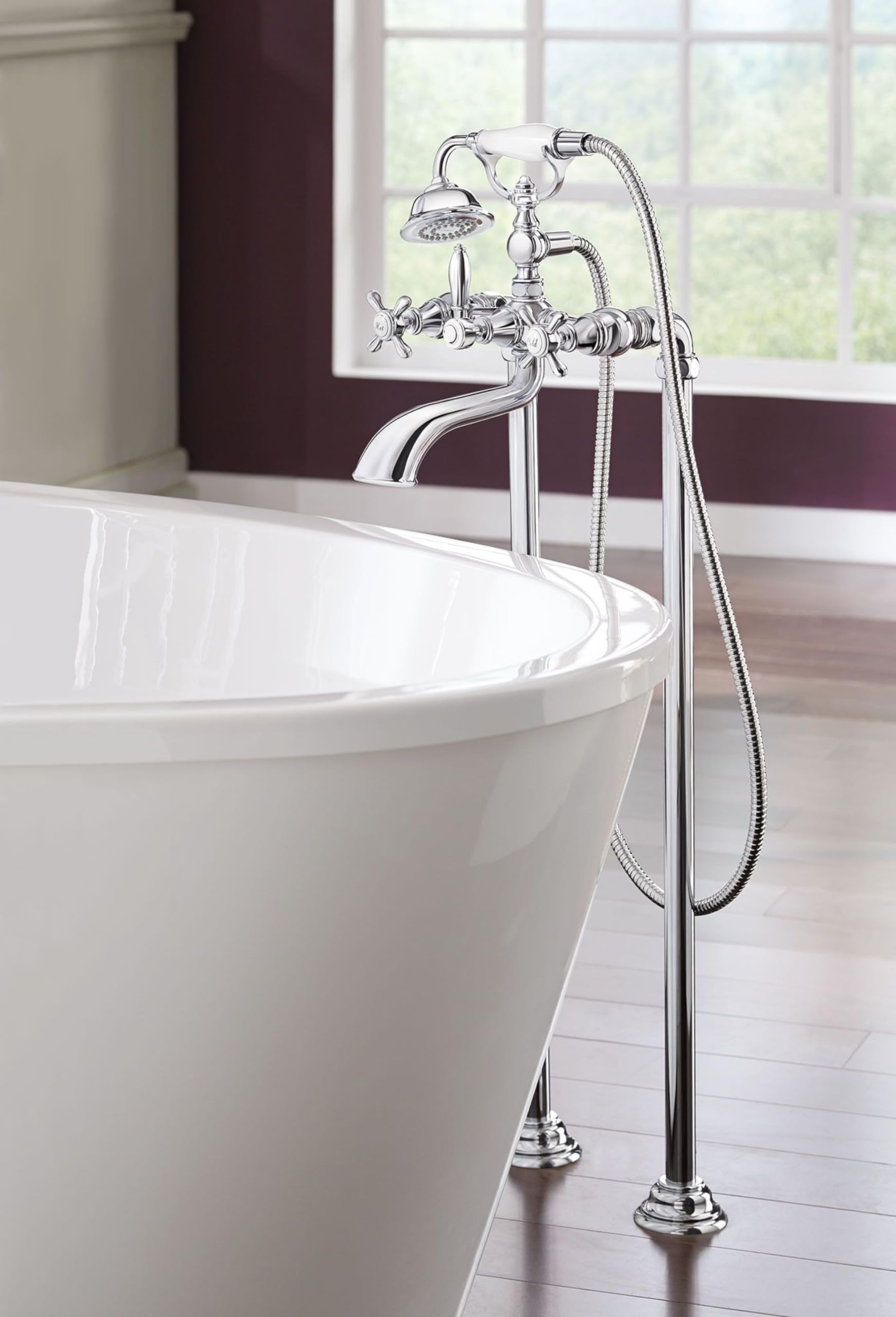 Chrome two-handle freestanding tub filler with curved spout, handheld shower, and floor-mounted risers positioned next to whi