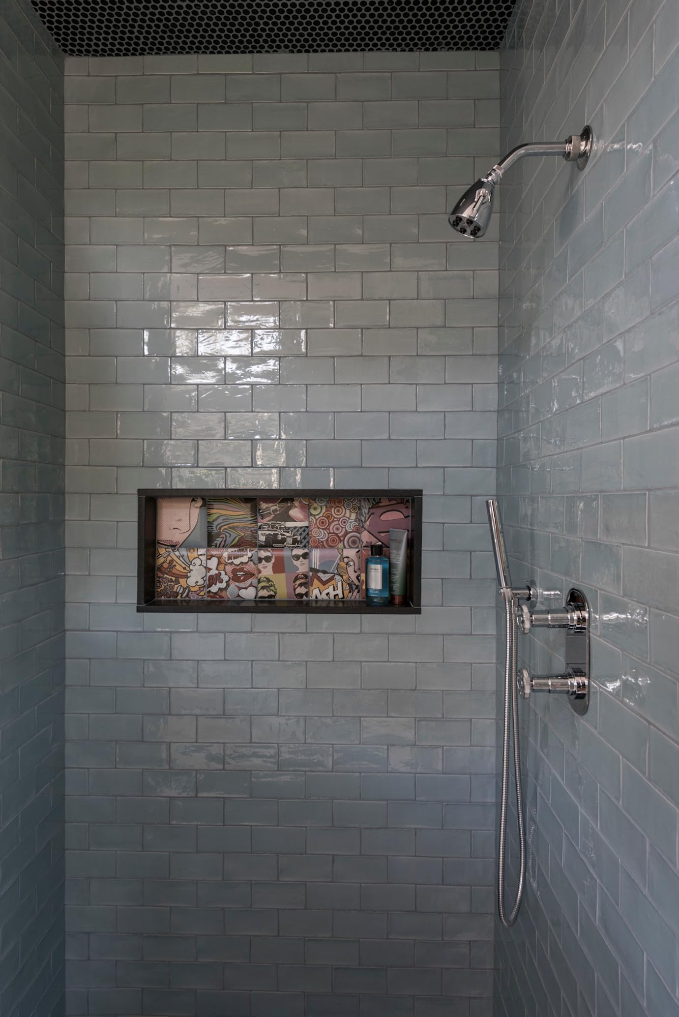 Polished chrome hand shower with curved arm mounted on subway tile shower wall.