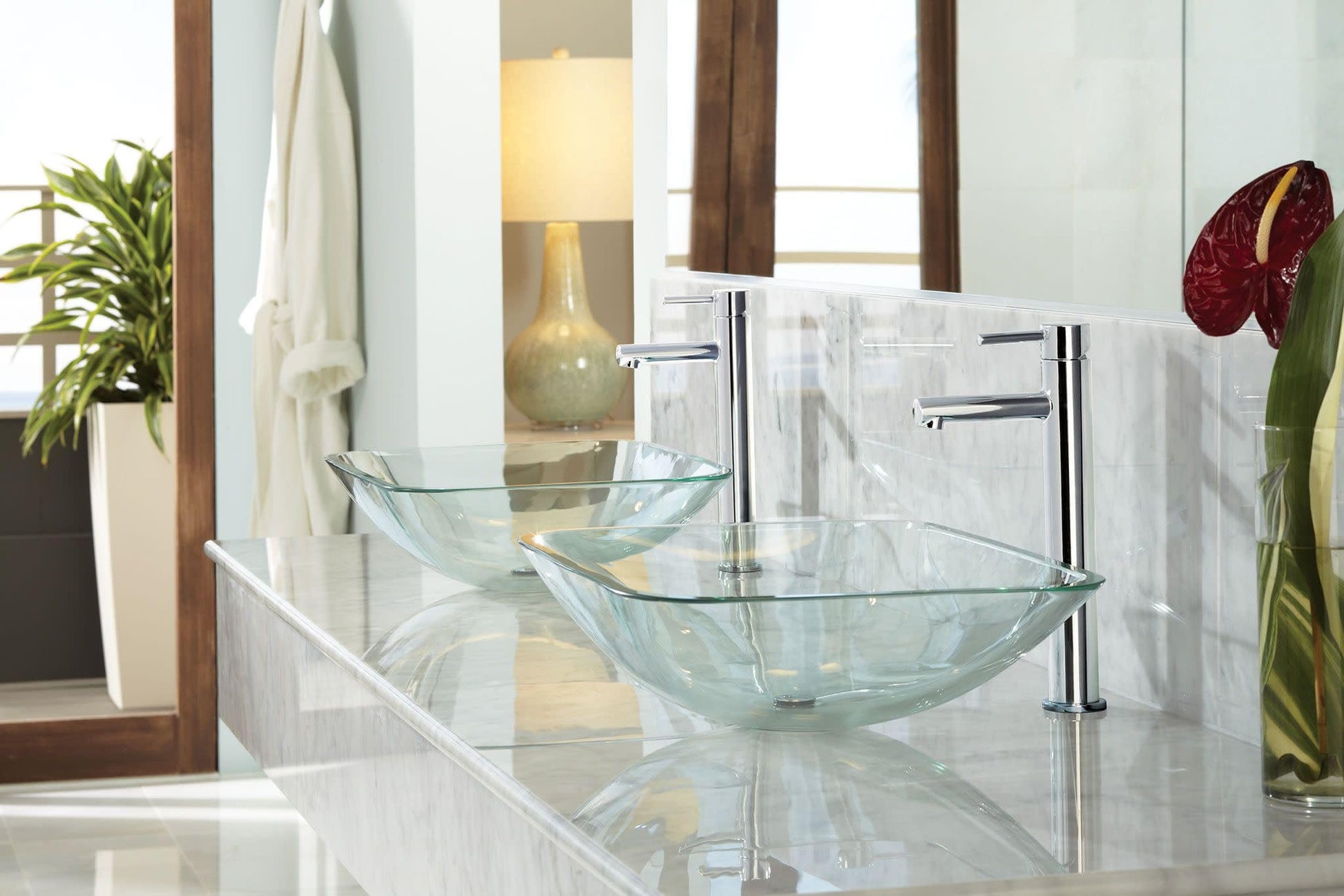 Brushed nickel single-handle faucet with curved spout mounted above two glass vessel sinks on marble countertop.