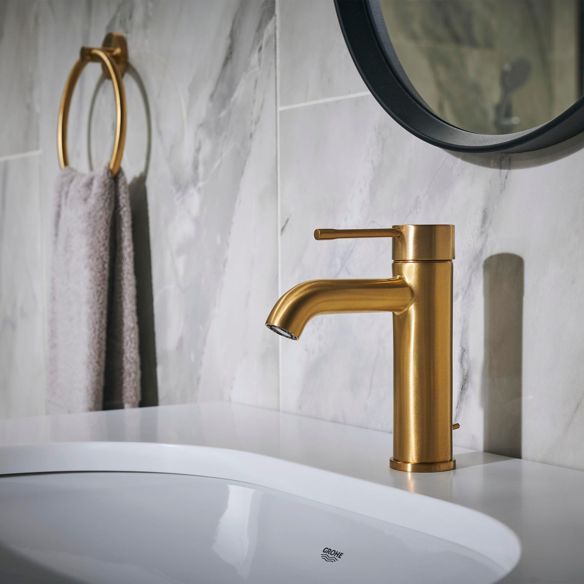 Grohe Essence brushed gold single-handle bathroom faucet with curved spout mounted on white countertop sink.