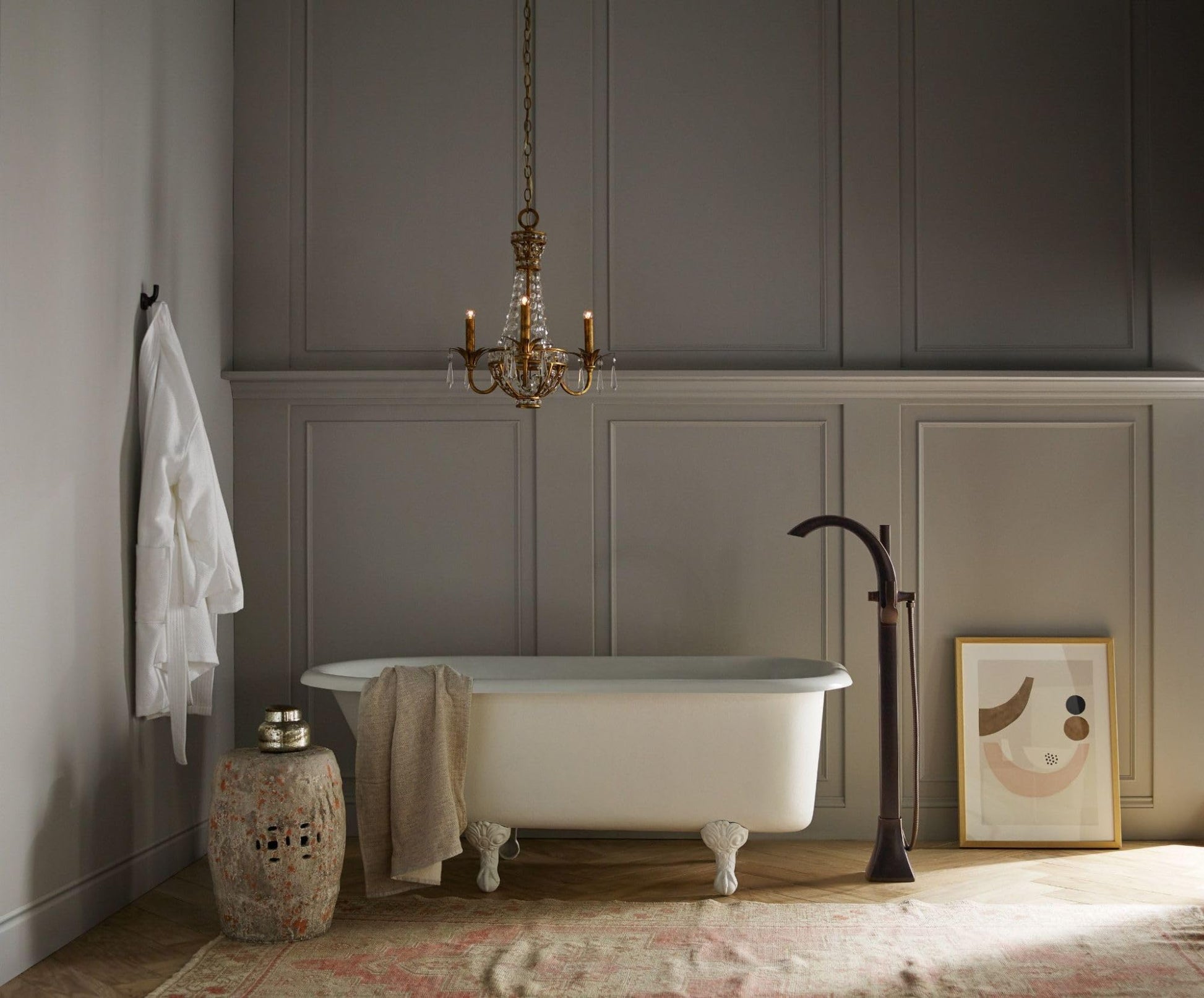 Oil rubbed bronze floor mount tub filler with single handle and detachable handshower standing beside white clawfoot bathtub.